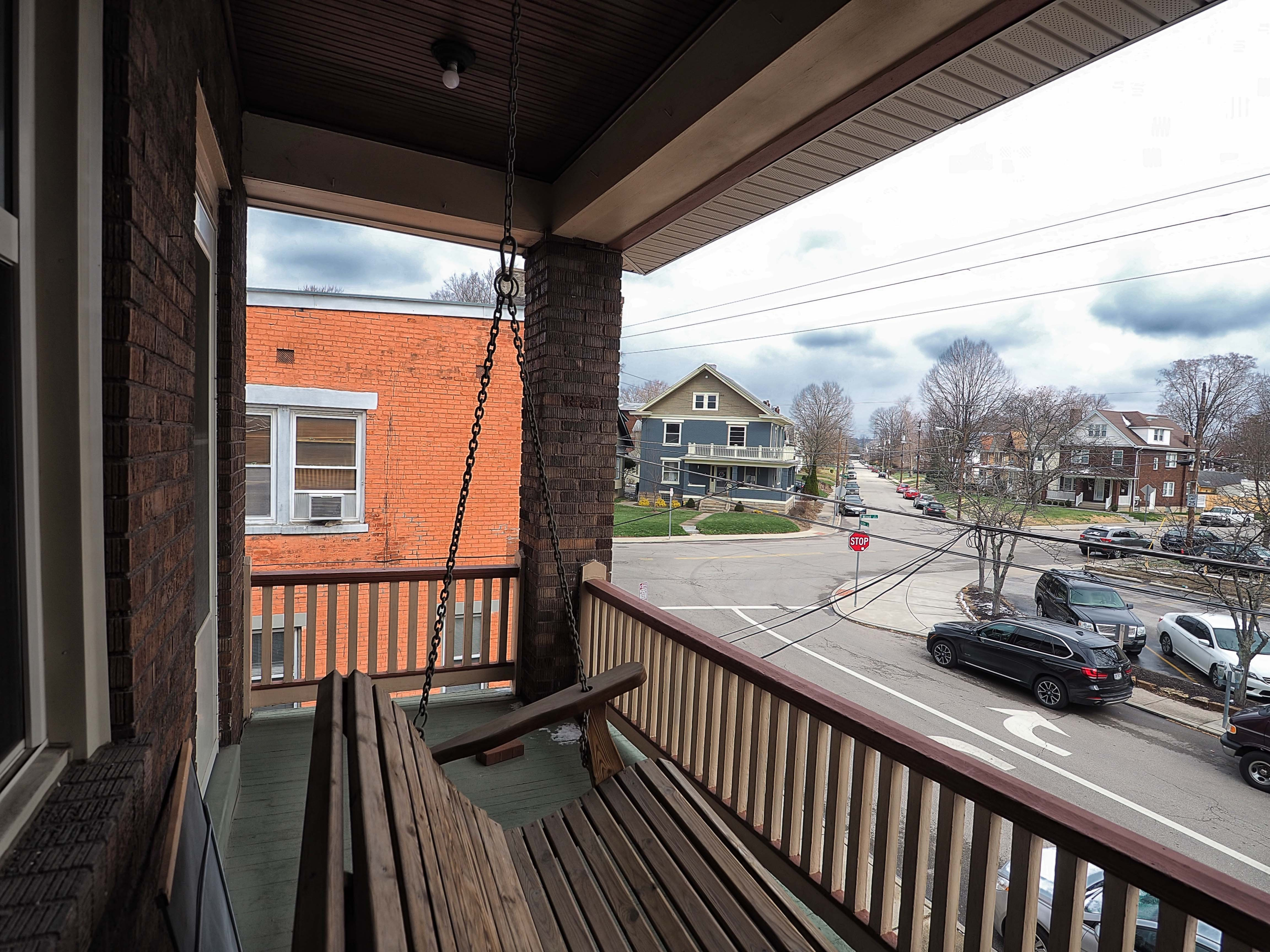 Charming apartment balcony with wooden swing, offering a cozy spot overlooking a vibrant neighborhood street view.