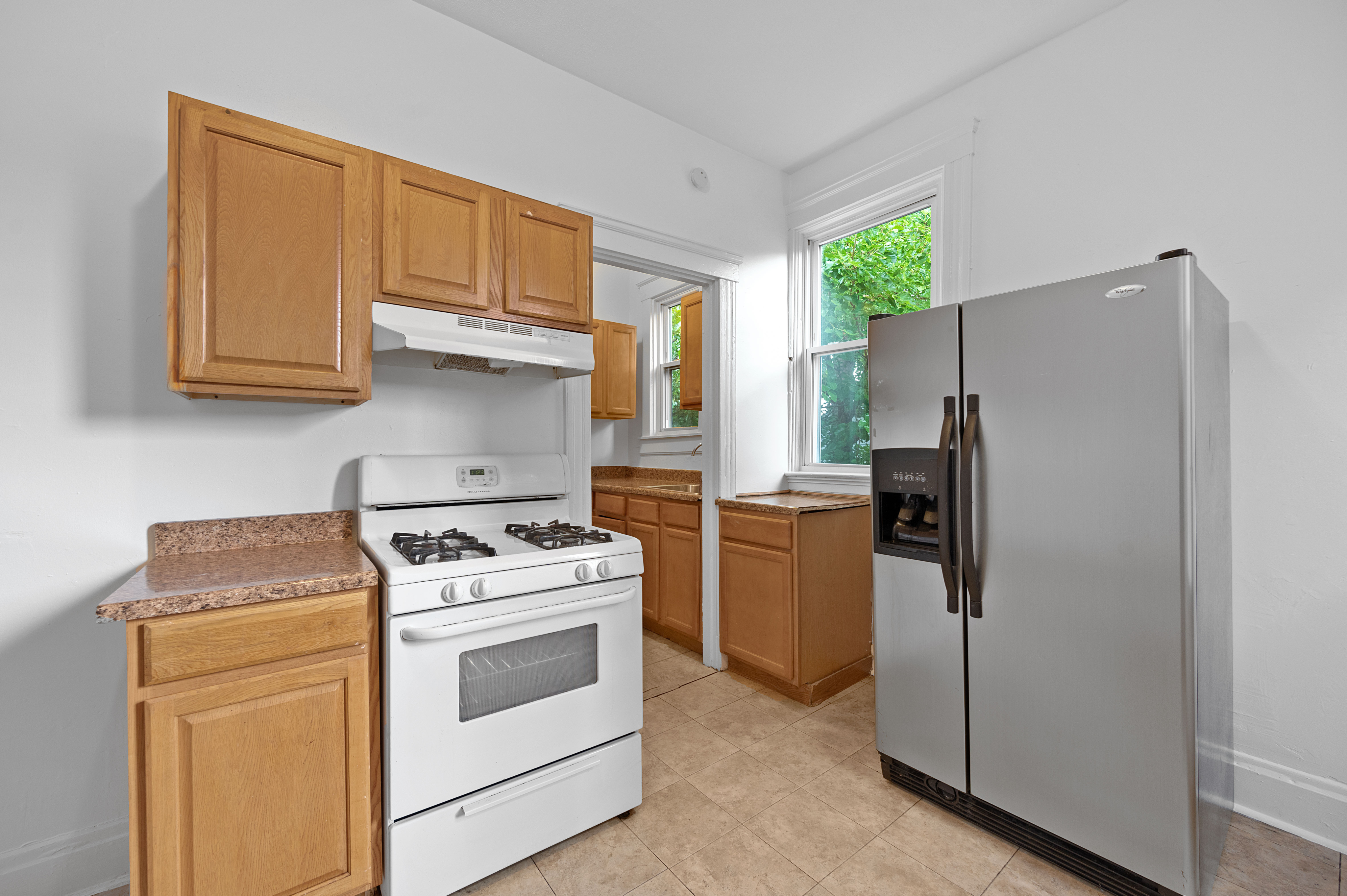 Modern kitchen with sleek stainless steel refrigerator, gas stove, and natural wood cabinetry, offering a bright and functional space.