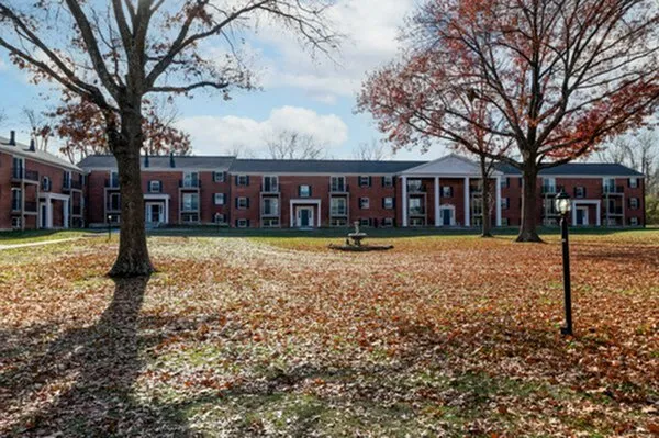 Charming apartment building with classic brick facade surrounded by lush autumn scenery and mature trees.