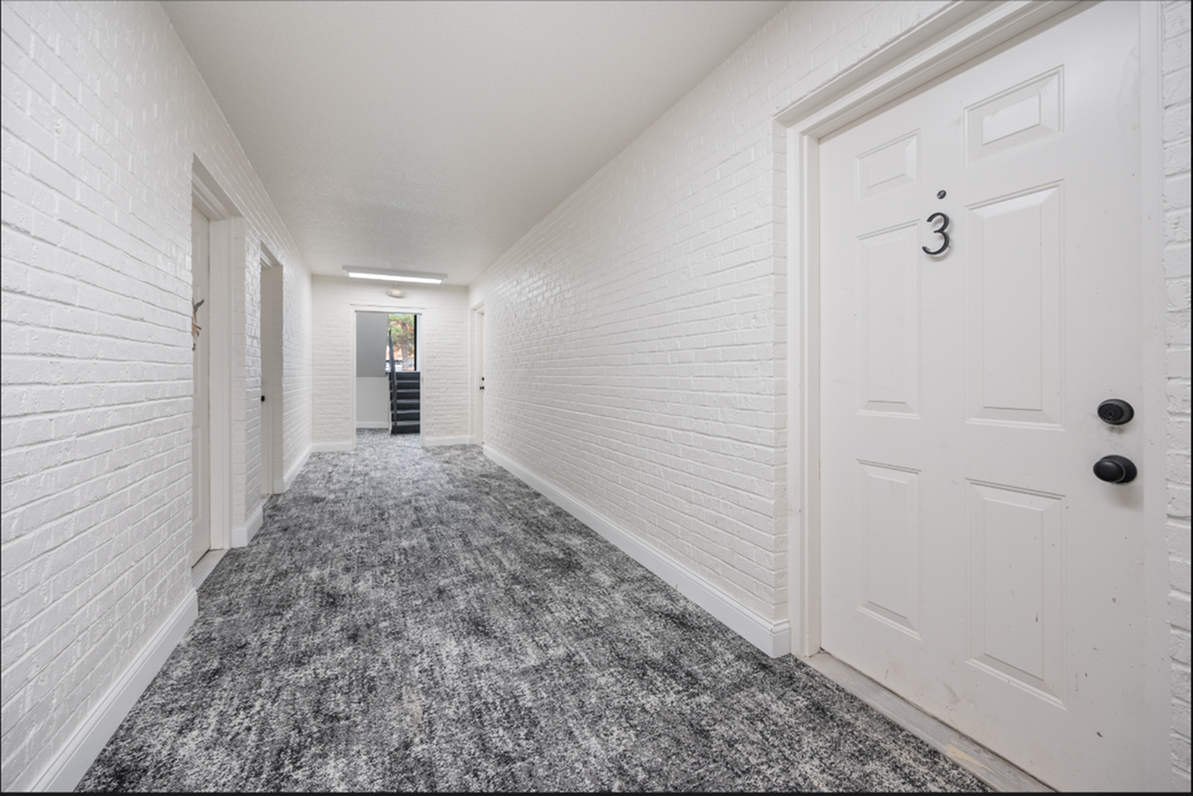 Modern apartment hallway with sleek white brick walls and plush gray carpeting leading to staircase.