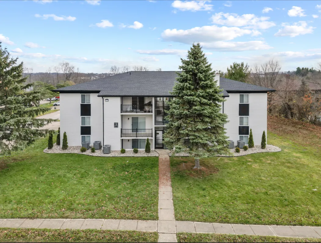 Charming apartment building with a modern exterior, surrounded by lush greenery and a welcoming path, ideal for cozy suburban living.