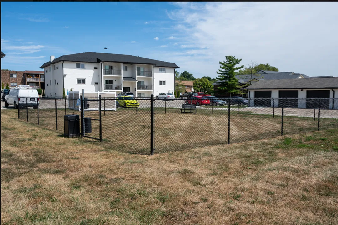 Charming white apartment building with spacious balconies, surrounded by greenery and ample parking area.