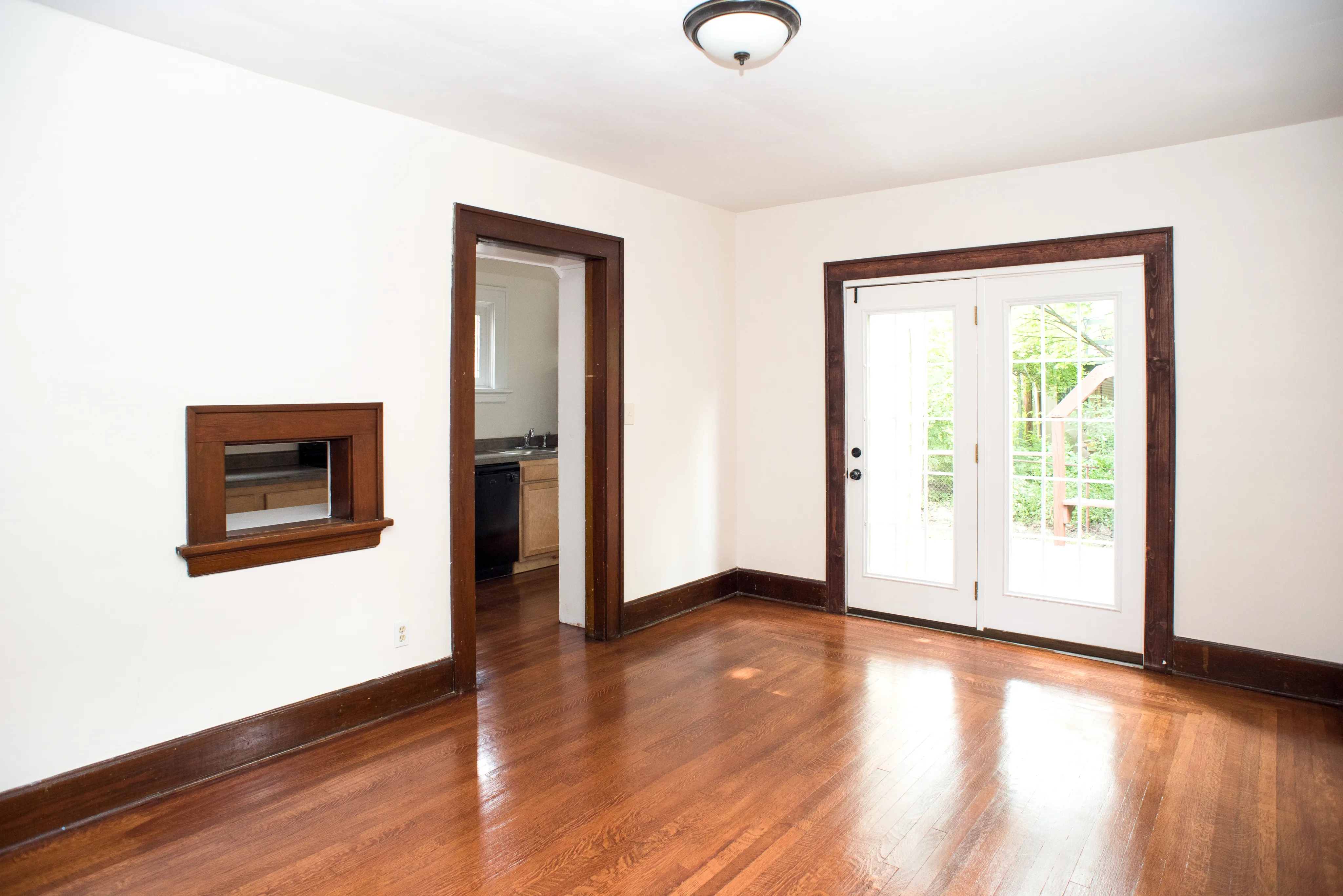 Bright and inviting room with polished hardwood floors, classic dark wood trim, and elegant French doors opening to natural surroundings.