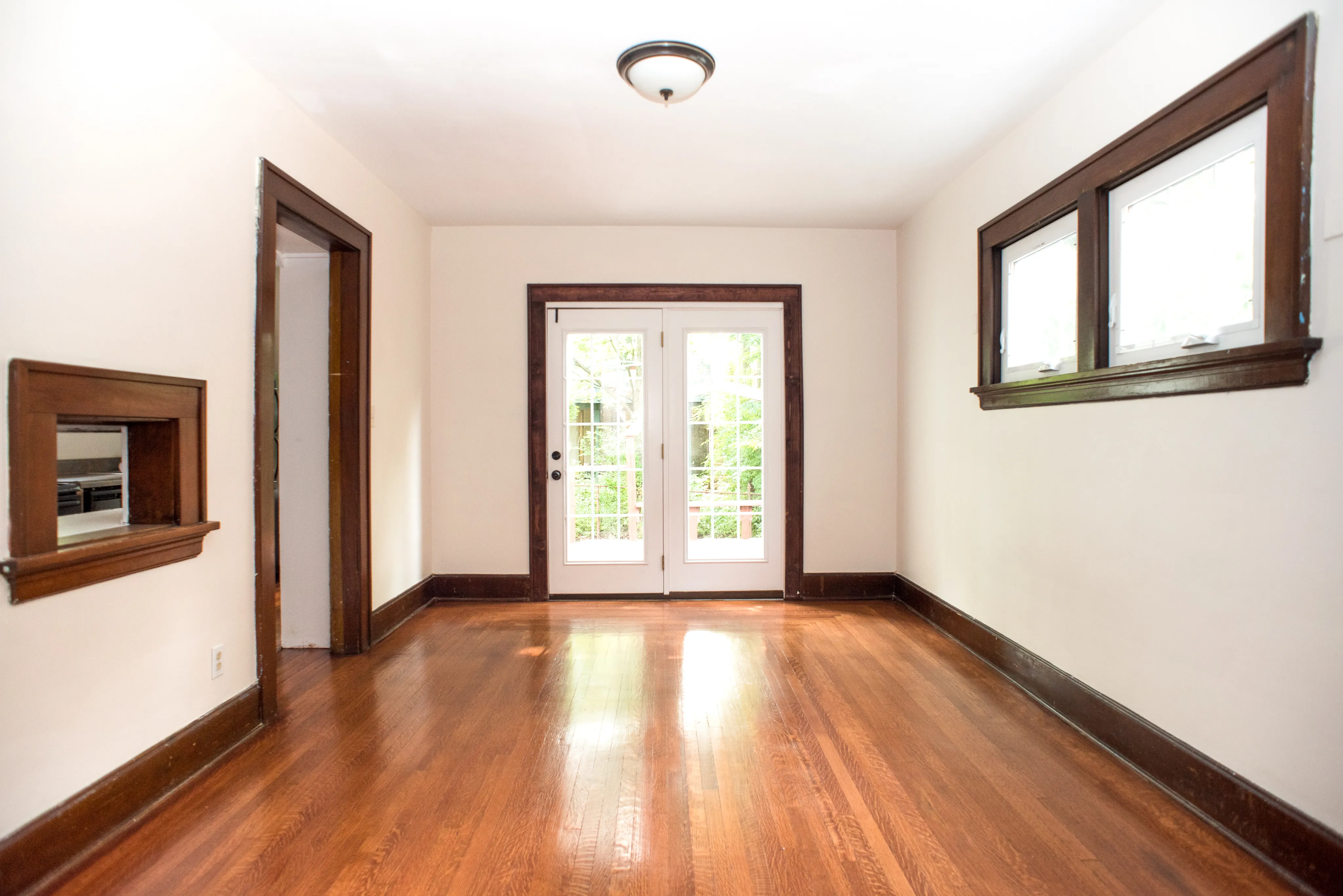 Bright and inviting empty room with elegant hardwood flooring, large windows, and stylish French doors leading to a lush garden view.