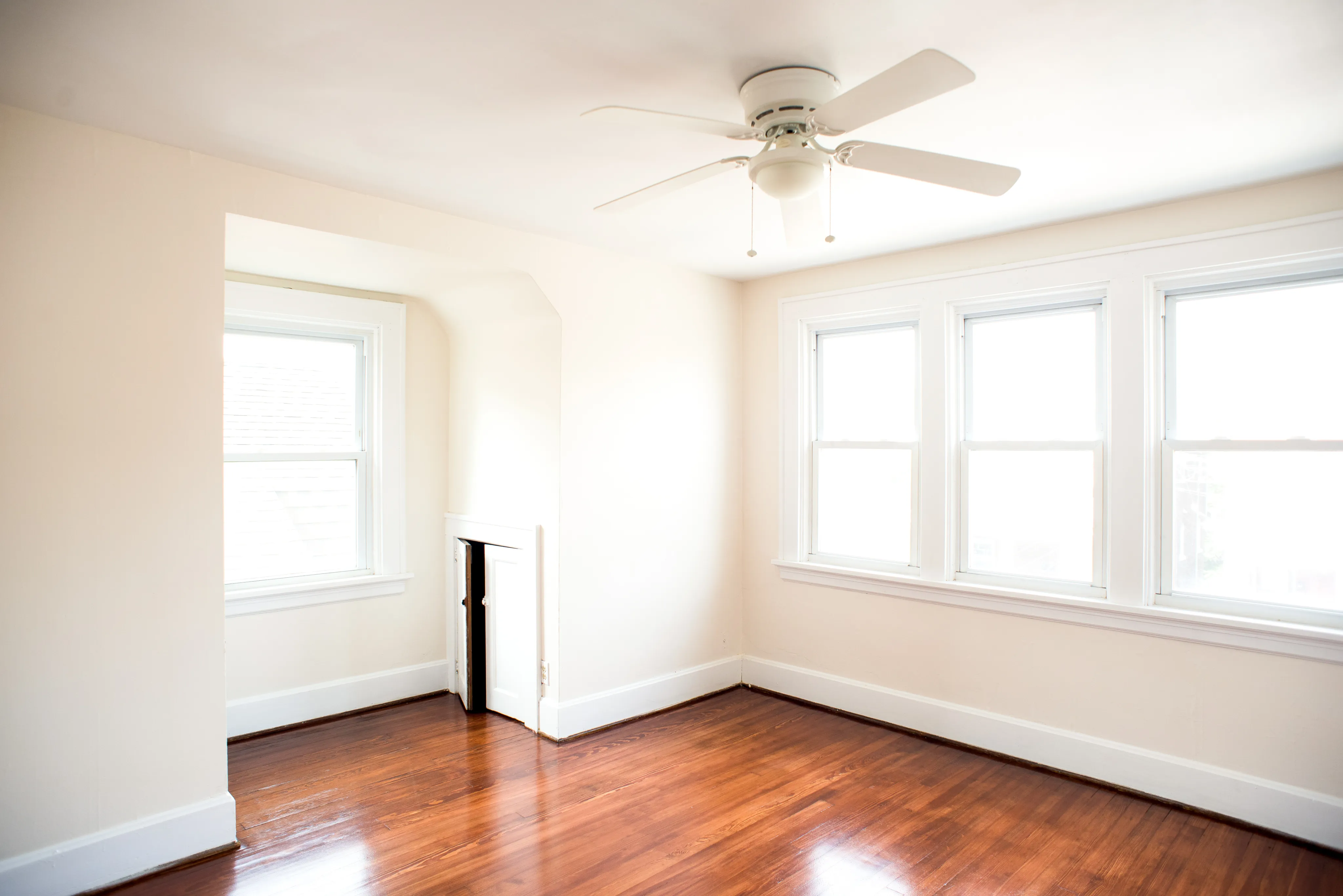 Bright room with polished hardwood floors, large windows, and a ceiling fan, offering a cozy and inviting atmosphere.