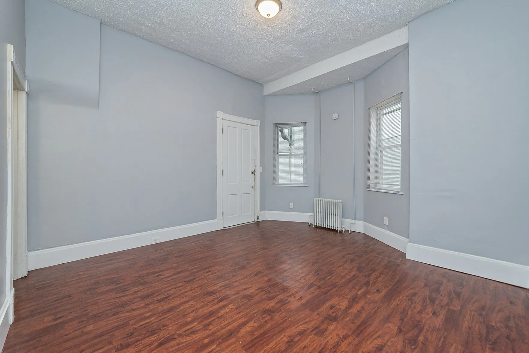 Bright and spacious room with elegant hardwood floors, soft gray walls, and ample natural light, ideal for creating a warm and inviting living space.