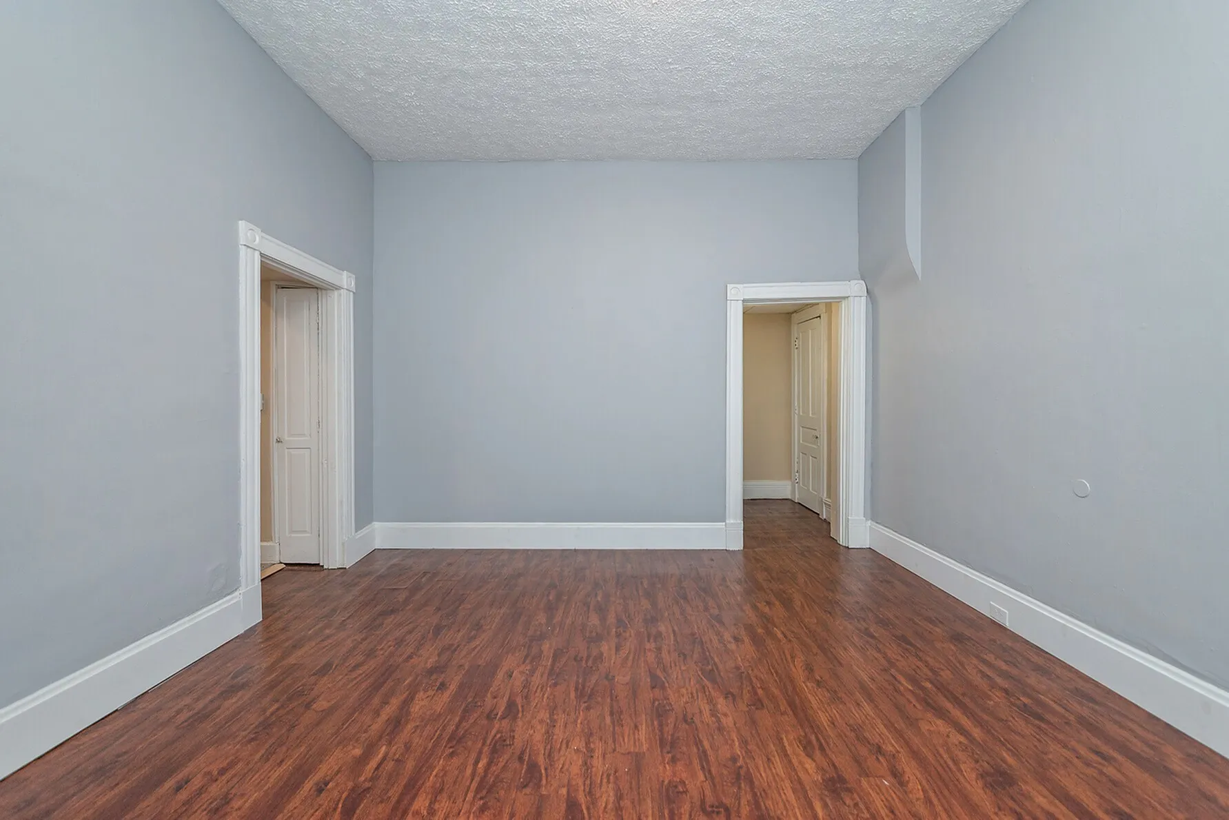 Bright and inviting room with sleek hardwood flooring, soft gray walls, and elegant white trim, offering a contemporary and versatile space.