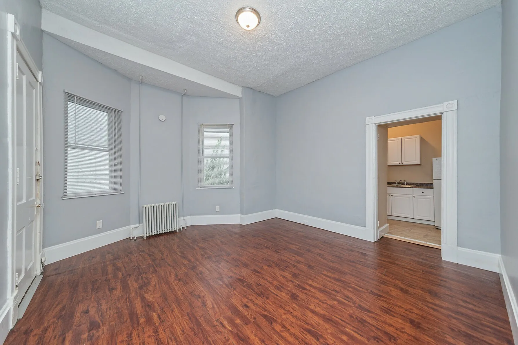 Bright and spacious living area with rich wooden floors and classic white trims, seamlessly connecting to a cozy kitchen.