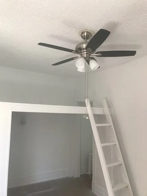 Charming loft-style room with a sleek ceiling fan and convenient ladder access to an elevated space, perfect for maximizing small spaces.