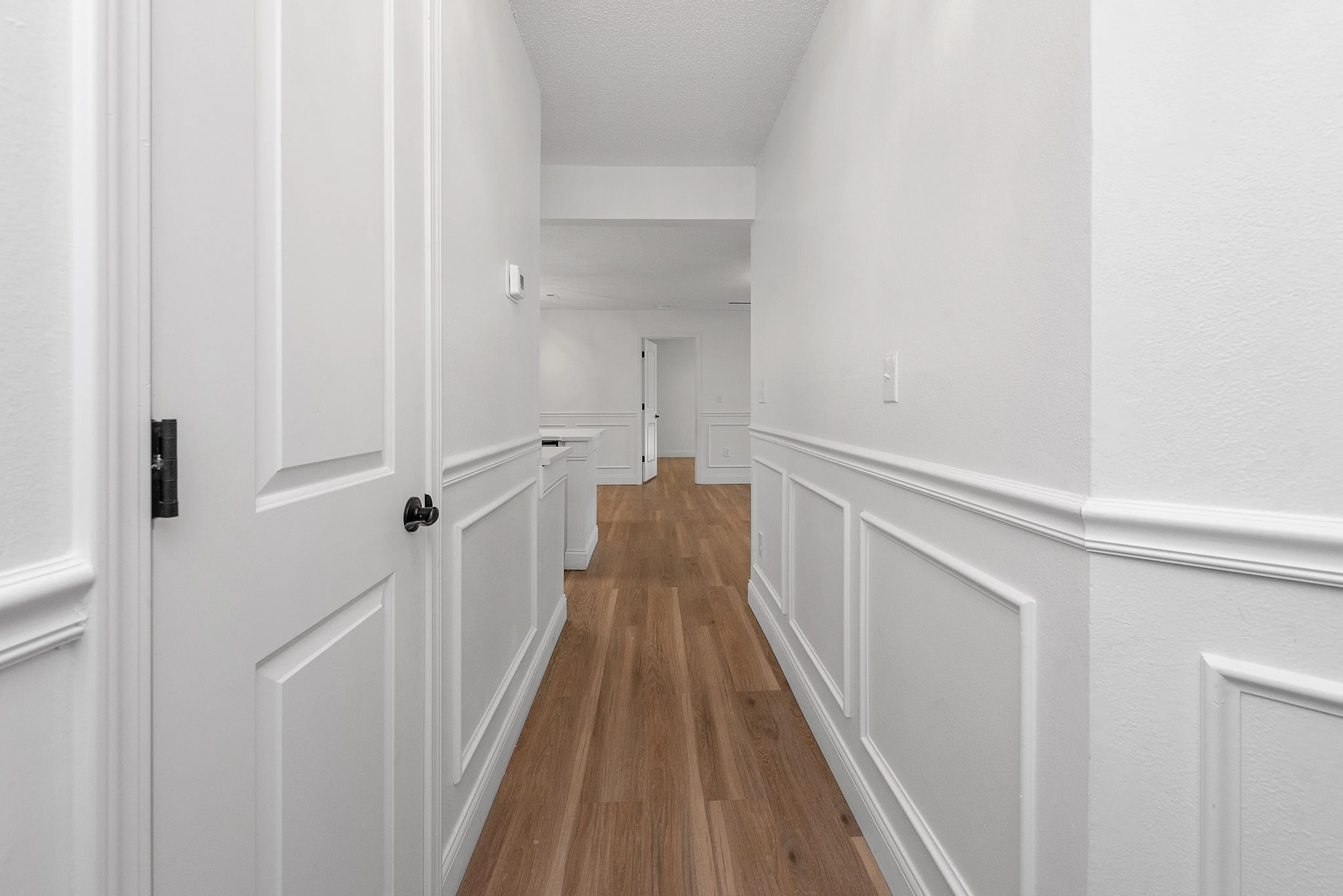 Bright and welcoming hallway with elegant white paneling and rich hardwood floors leading to open living spaces.