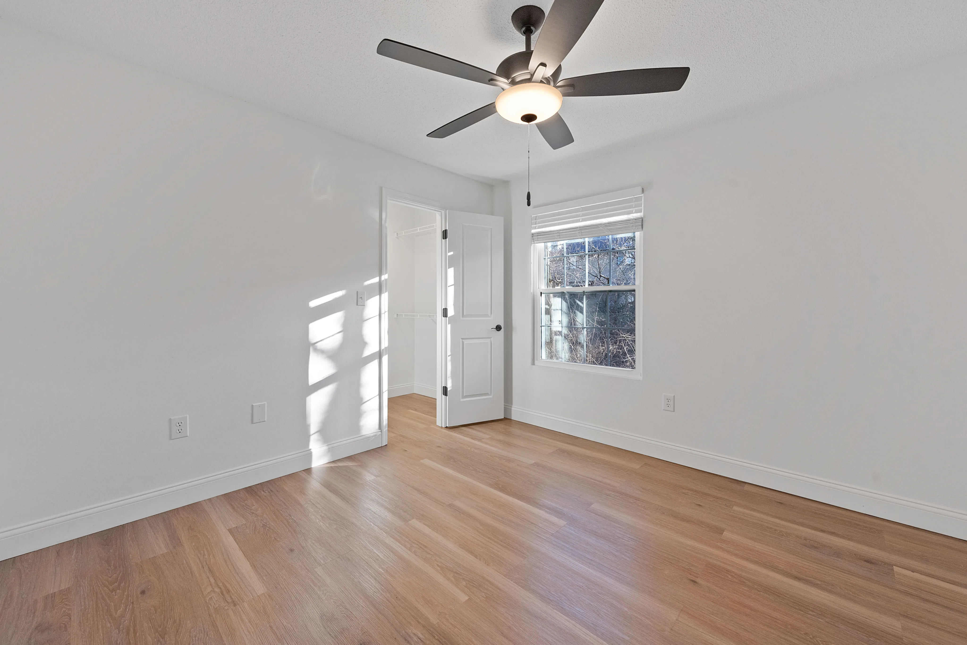 Bright and airy bedroom with natural light, featuring hardwood floors, ceiling fan, and a spacious closet.