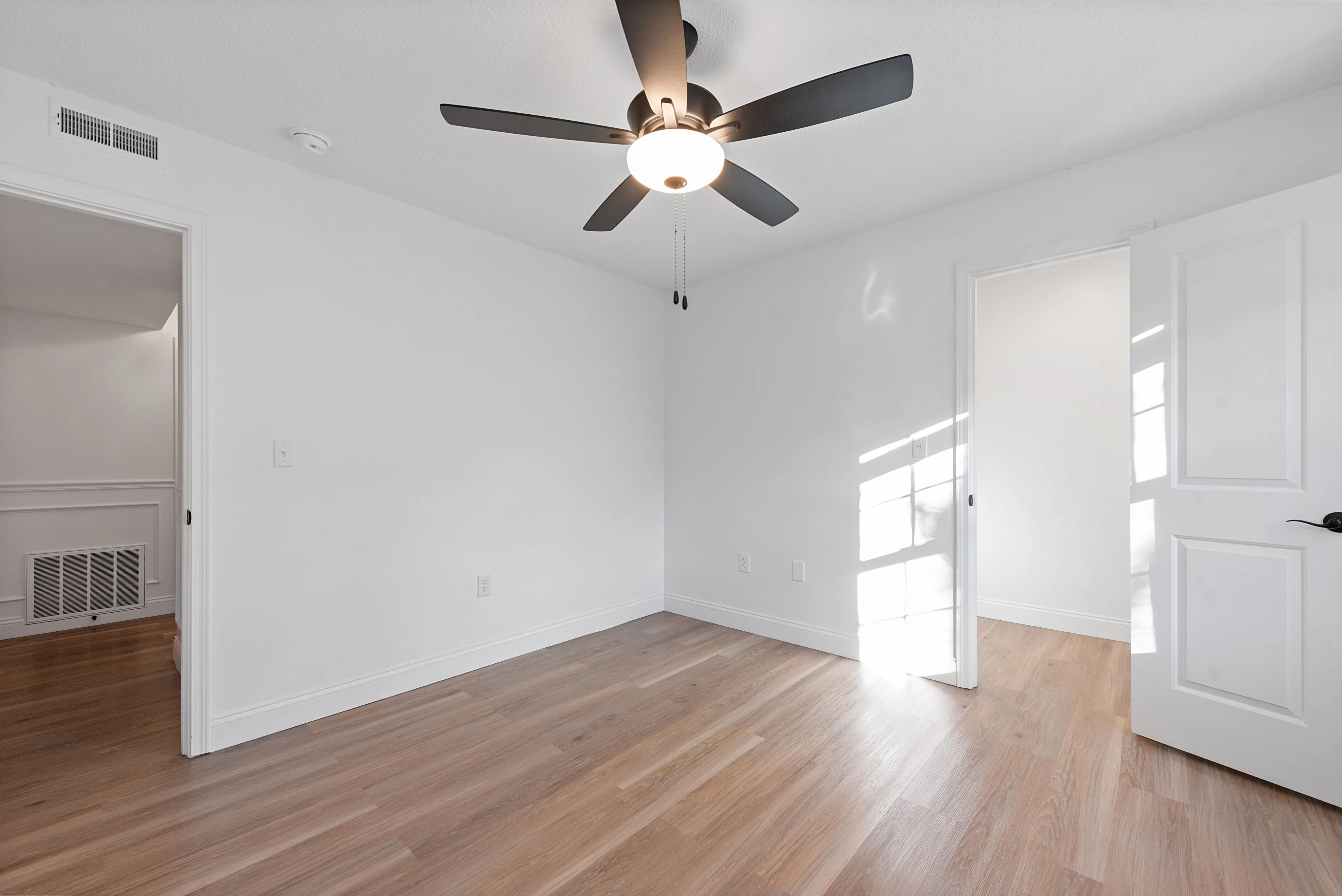 Bright and modern bedroom with elegant wood flooring and a sleek ceiling fan, offering ample natural light.