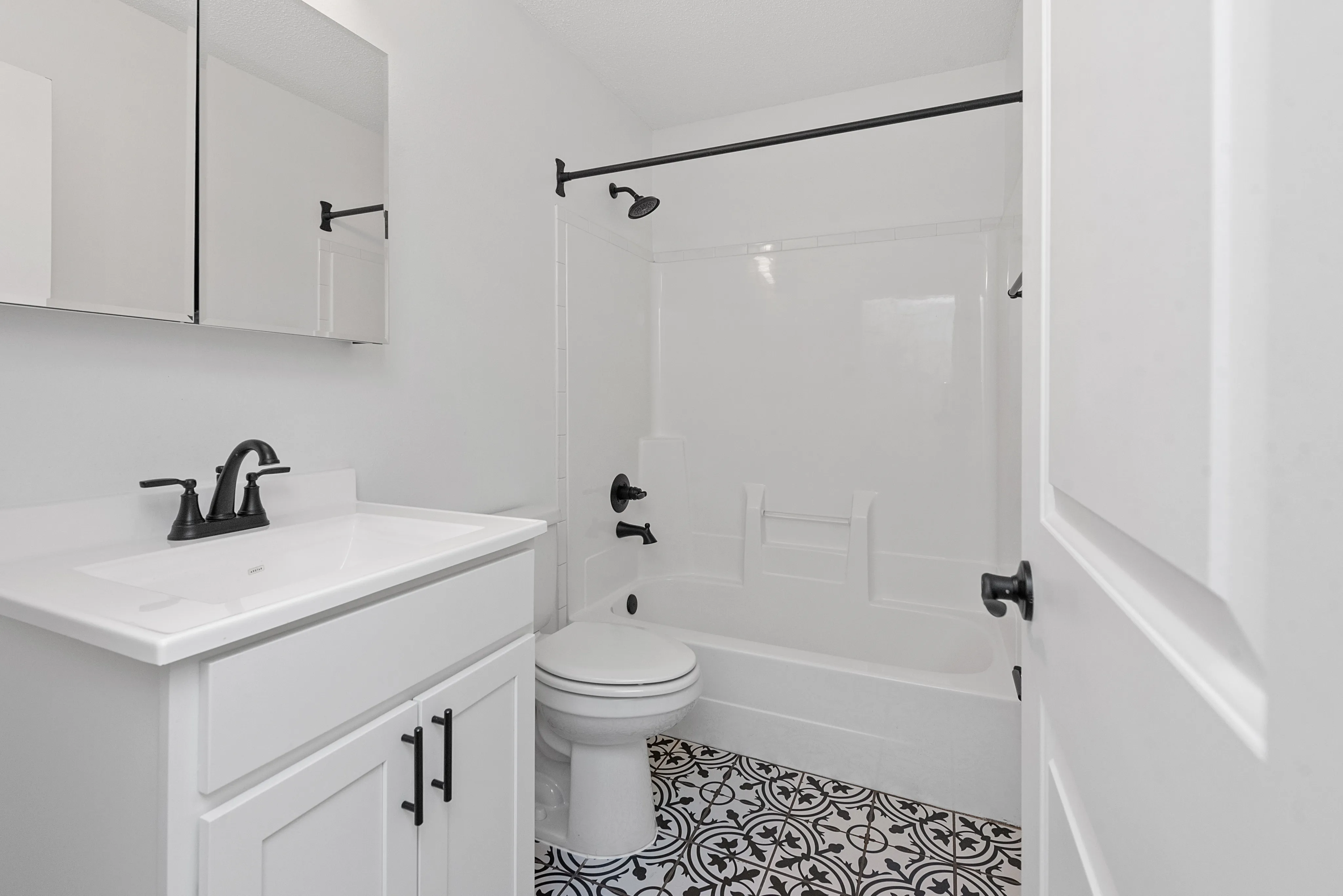 Modern bathroom with a sleek white vanity, stylish black fixtures, and elegant patterned tiles.