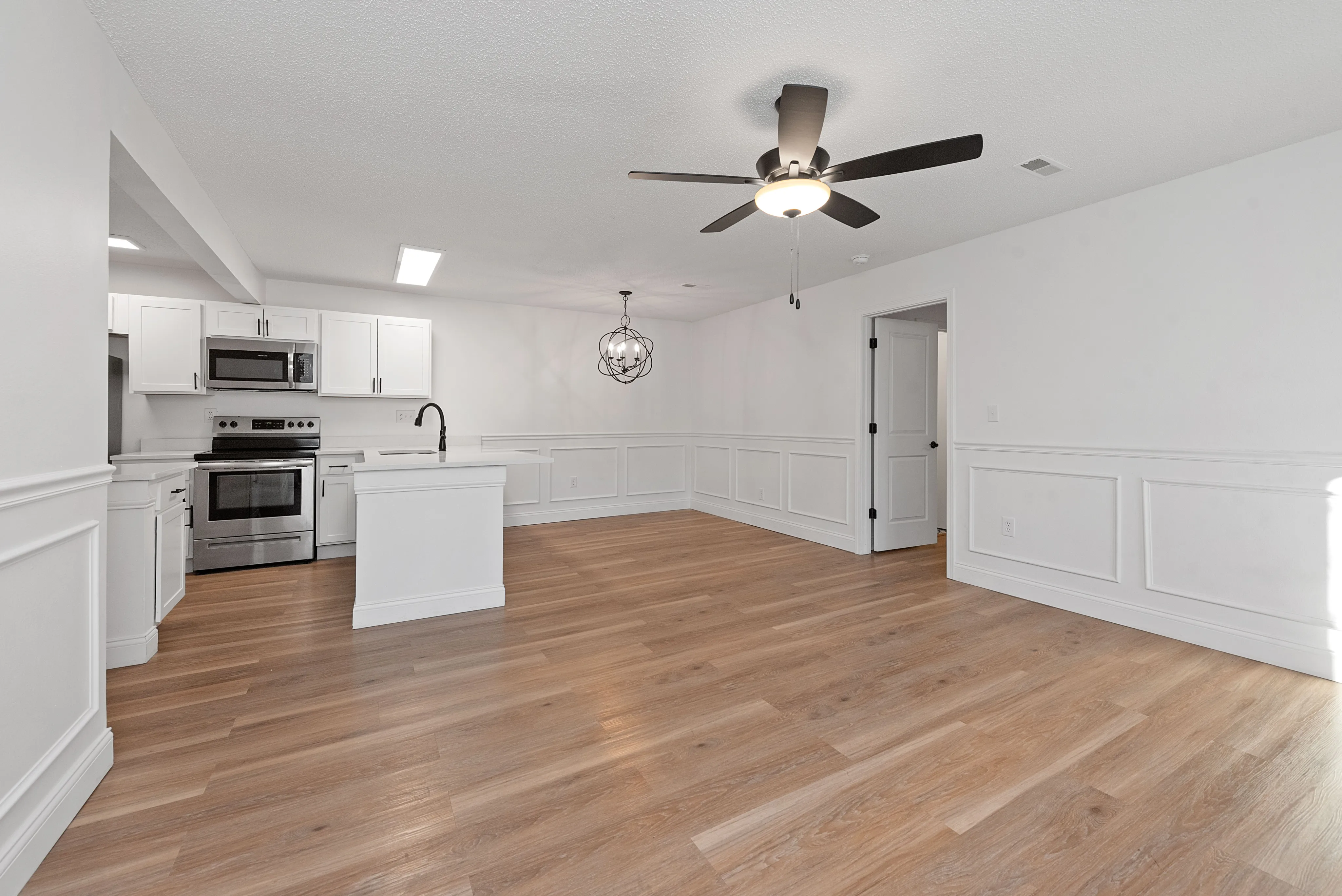 Modern open-concept kitchen and living area with sleek white cabinets, stainless steel appliances, elegant lighting, and warm wood flooring.