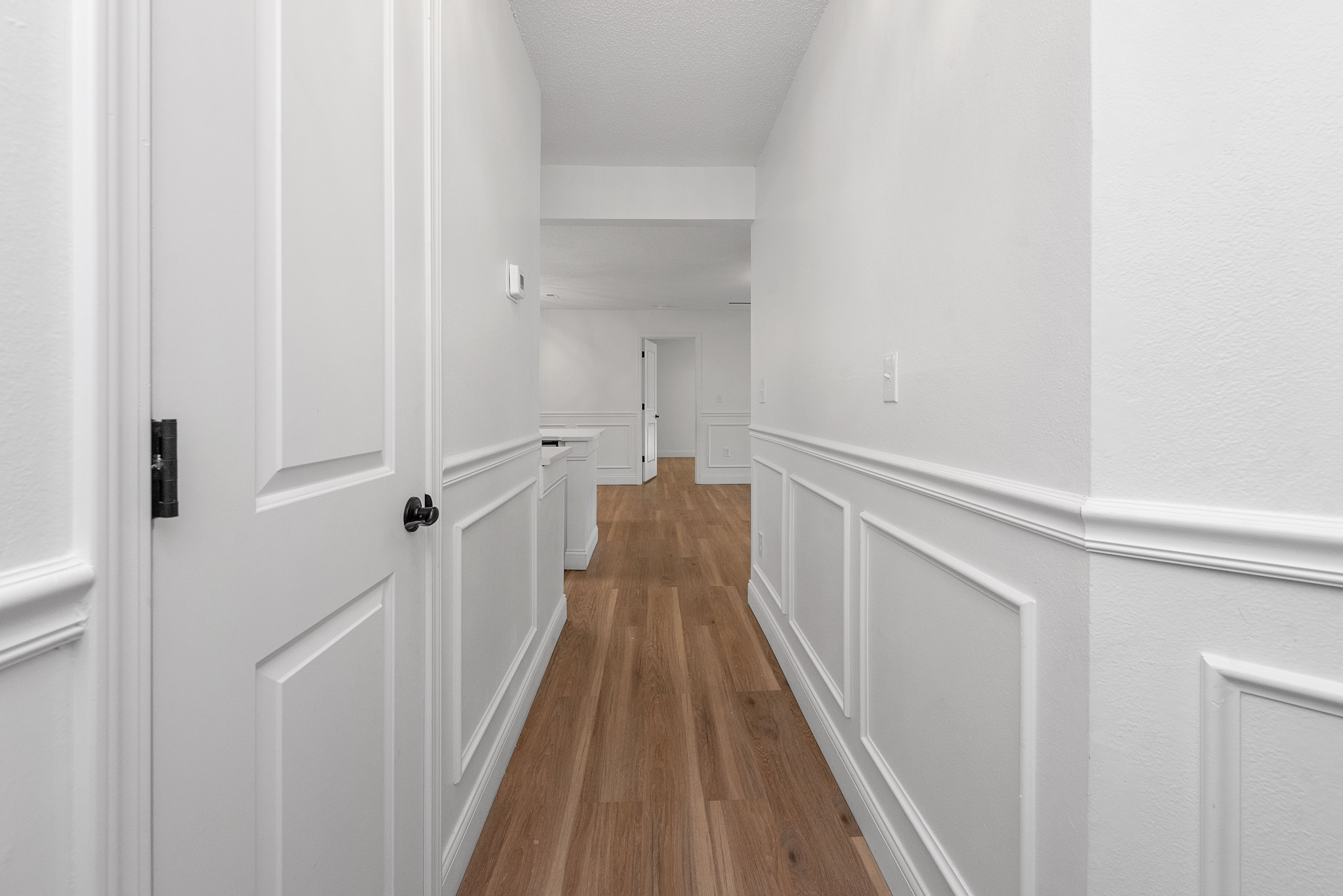 Elegant hallway with pristine white walls and warm wooden flooring, leading to a spacious living area.
