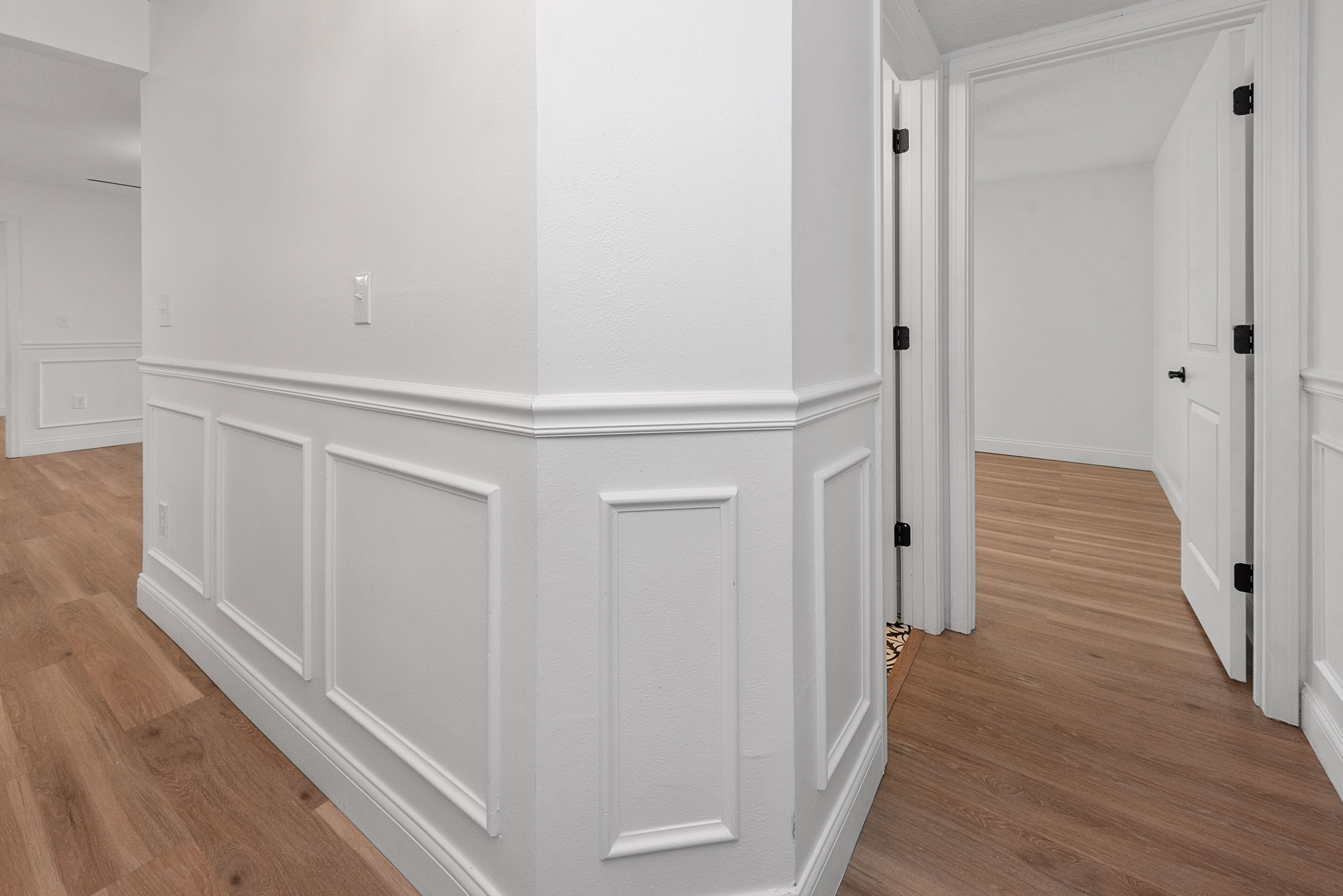 Elegant hallway with white paneling and premium wood flooring leading to two doorways.