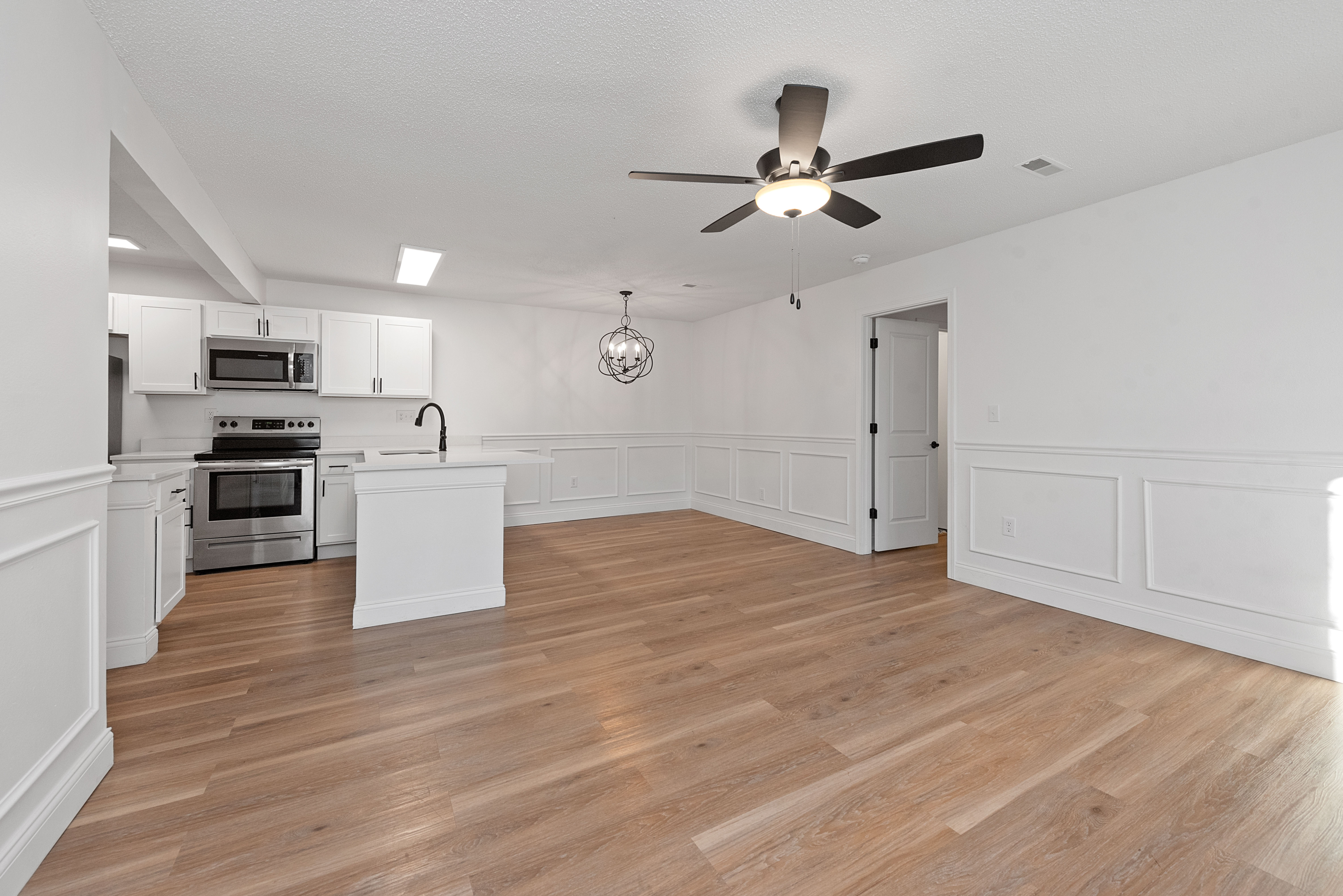 Chic open-plan living space with modern kitchen, elegant light fixture, and hardwood flooring.