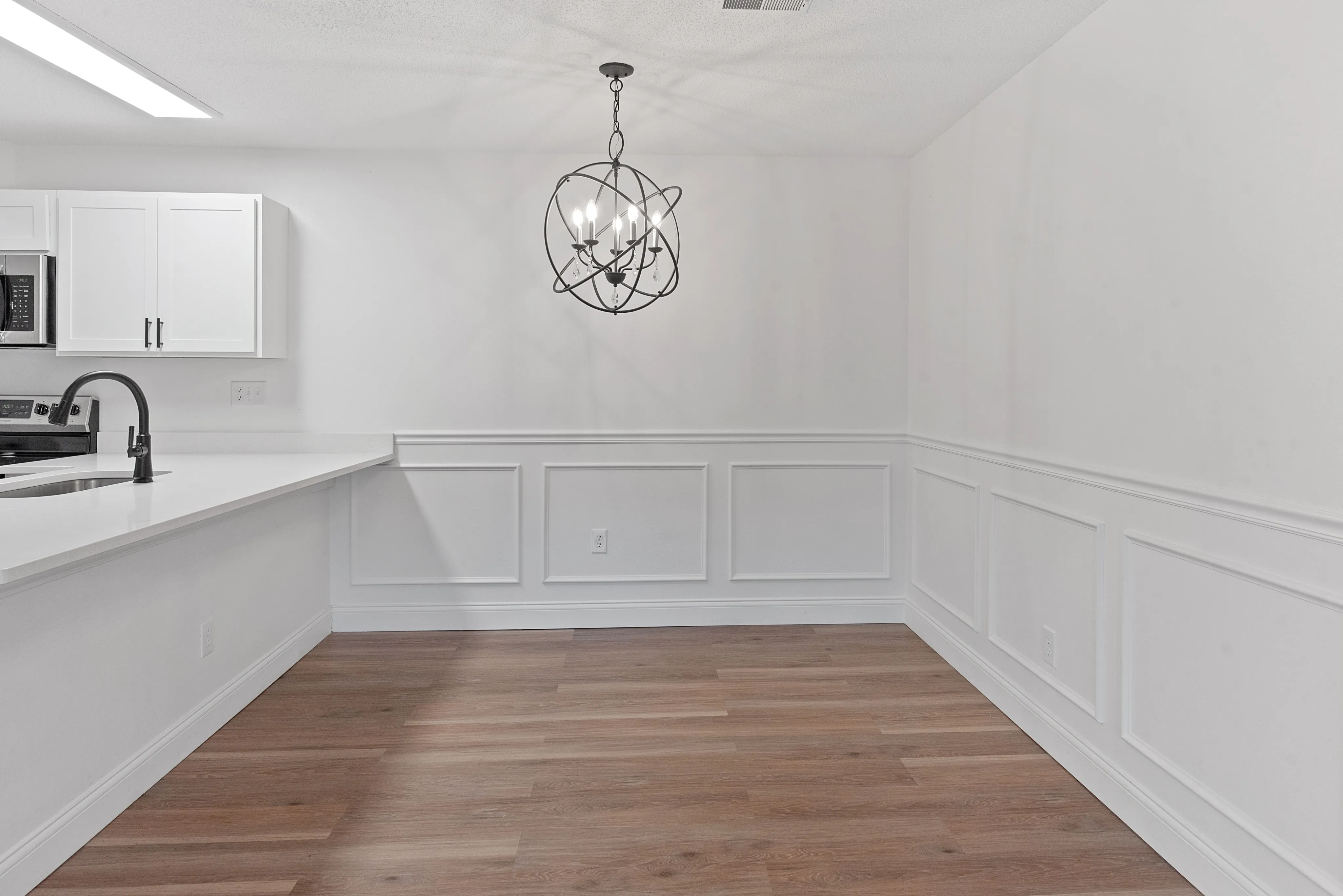 Elegant and modern kitchen featuring sleek white cabinetry, stylish light fixture, and warm wood flooring.
