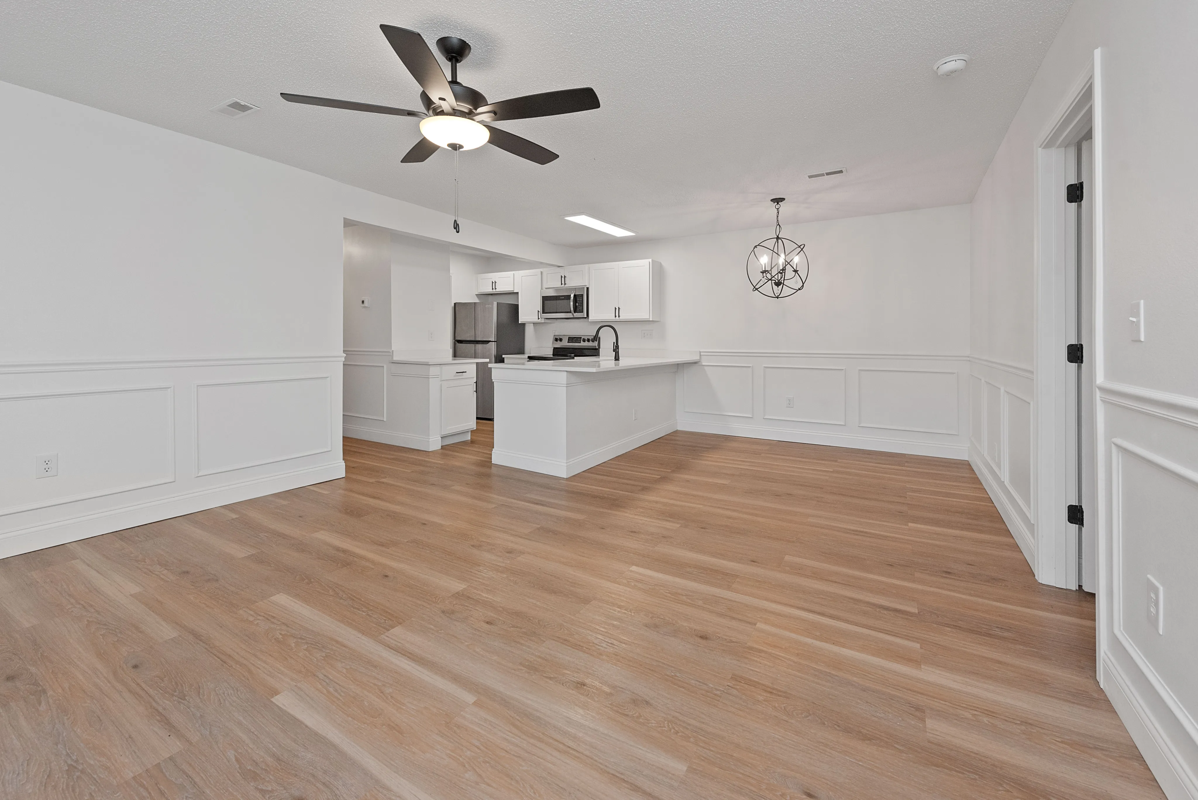 Modern open-concept living area with chic light fixtures, sleek wood flooring, and a stylish kitchen featuring stainless steel appliances.