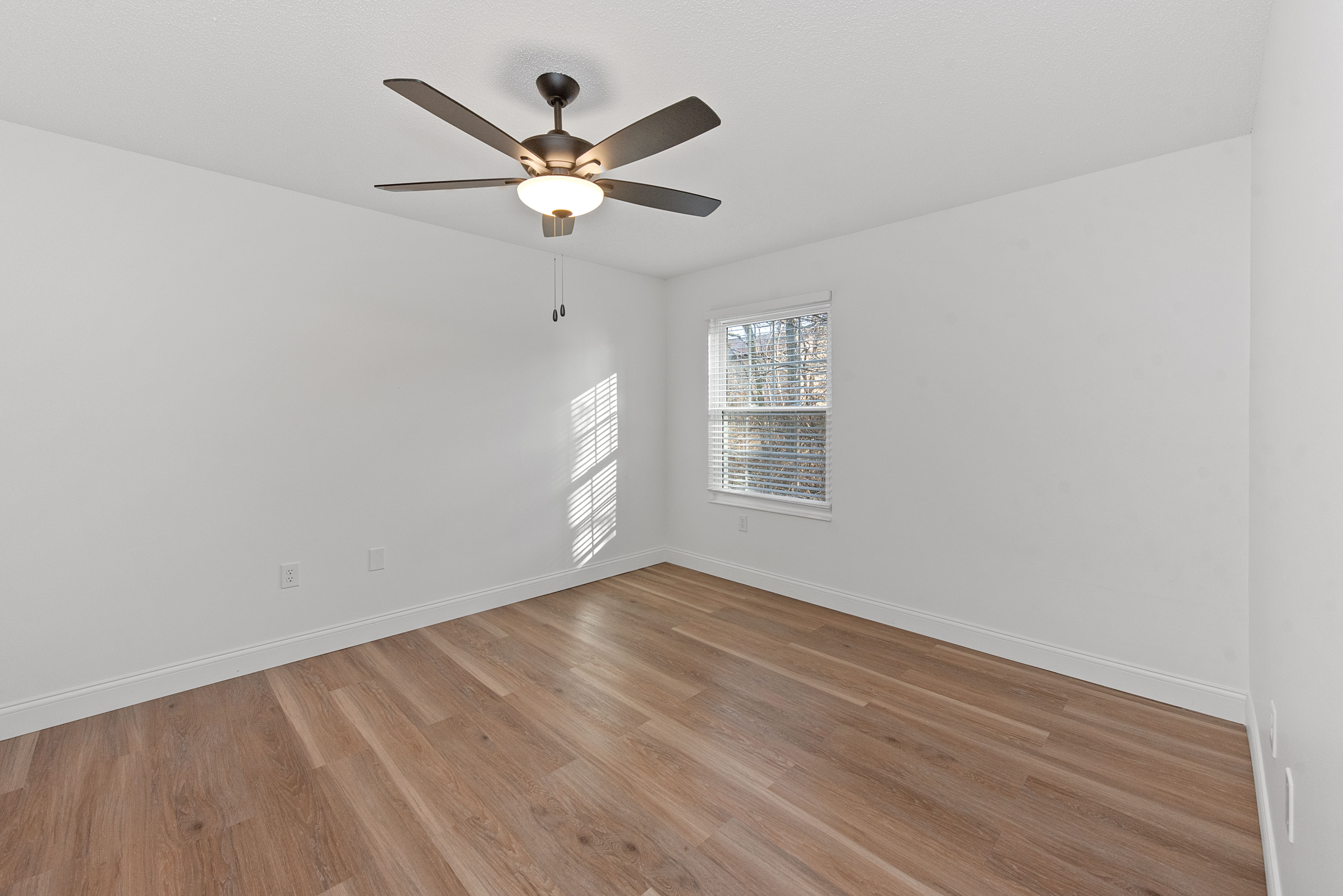 Bright and airy bedroom with hardwood flooring, ceiling fan, and natural light from a large window.