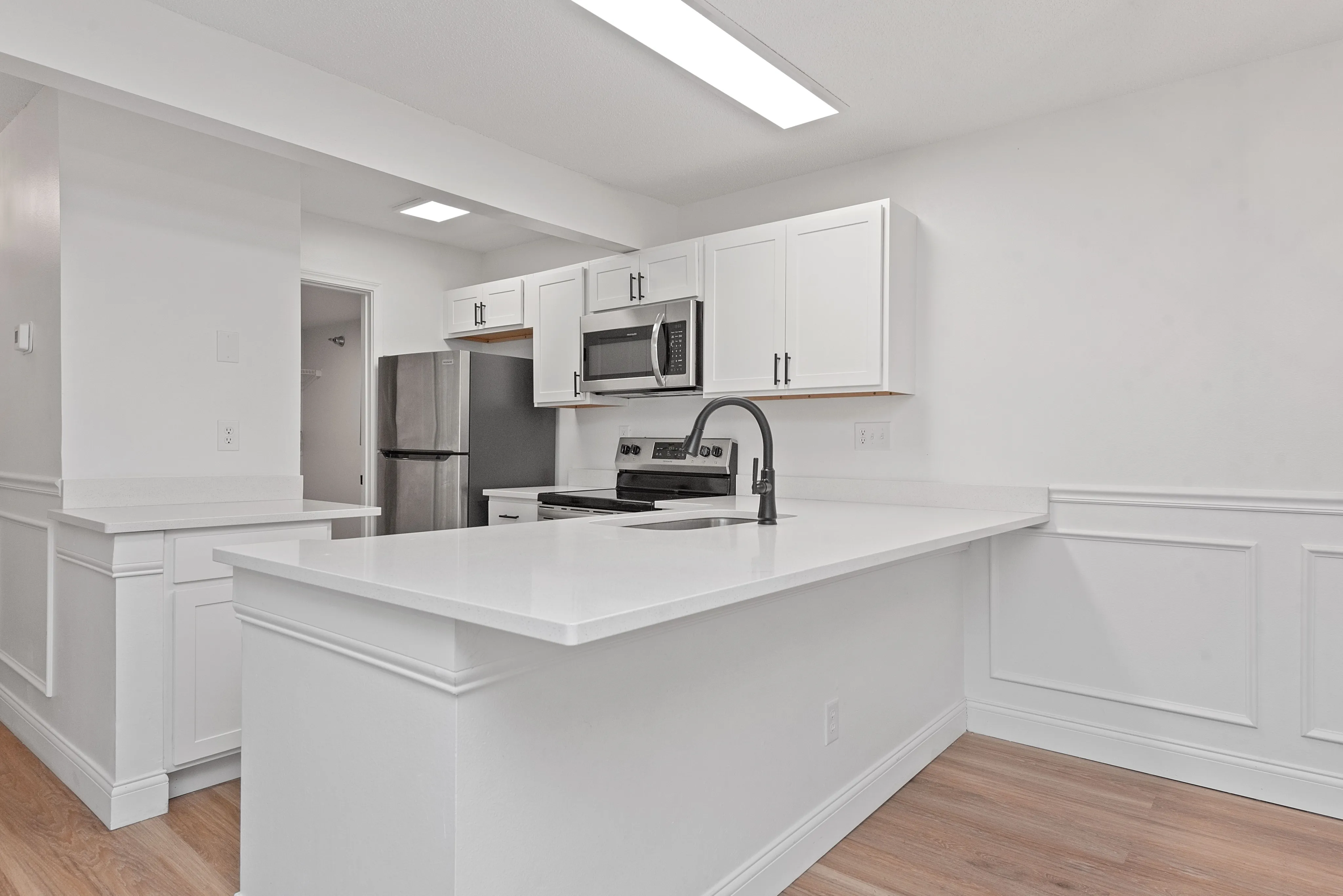 Bright modern kitchen with sleek white cabinetry, stainless steel appliances, and elegant hardwood floors.