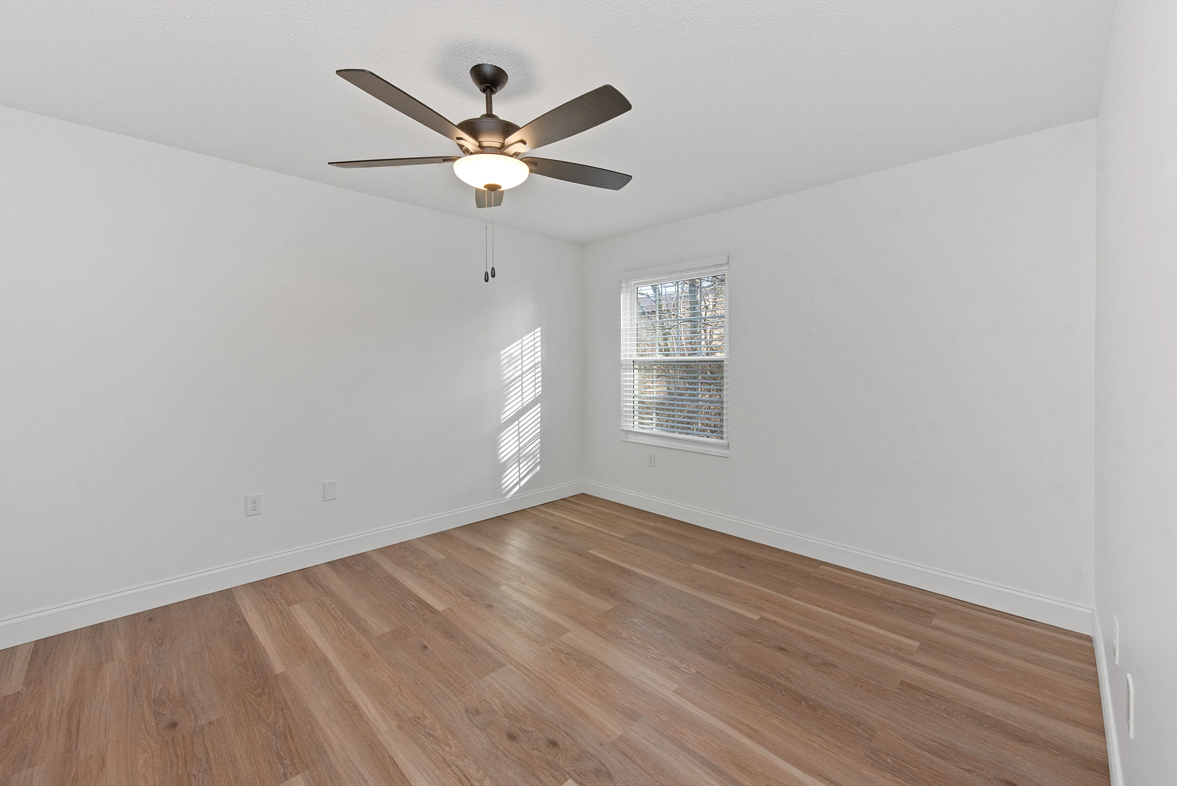 Bright and airy bedroom featuring elegant hardwood floors and a modern ceiling fan, perfect for a cozy retreat.