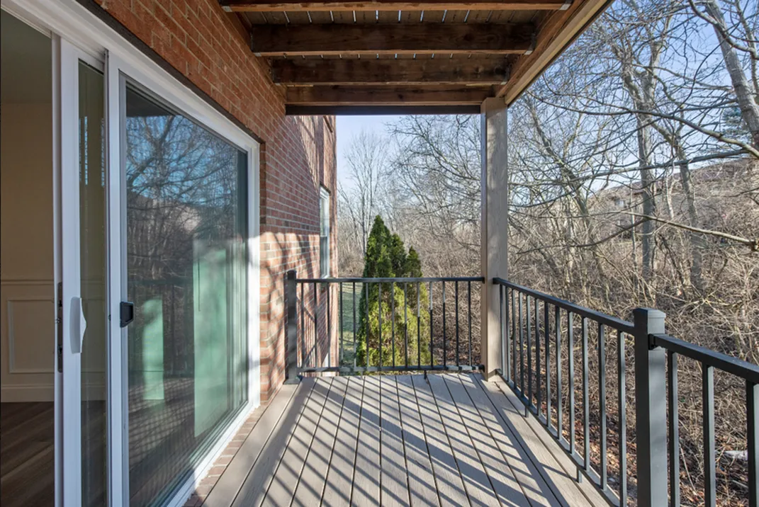 Charming apartment balcony with natural wood accents, overlooking serene wooded area and featuring ample outdoor space for relaxation.