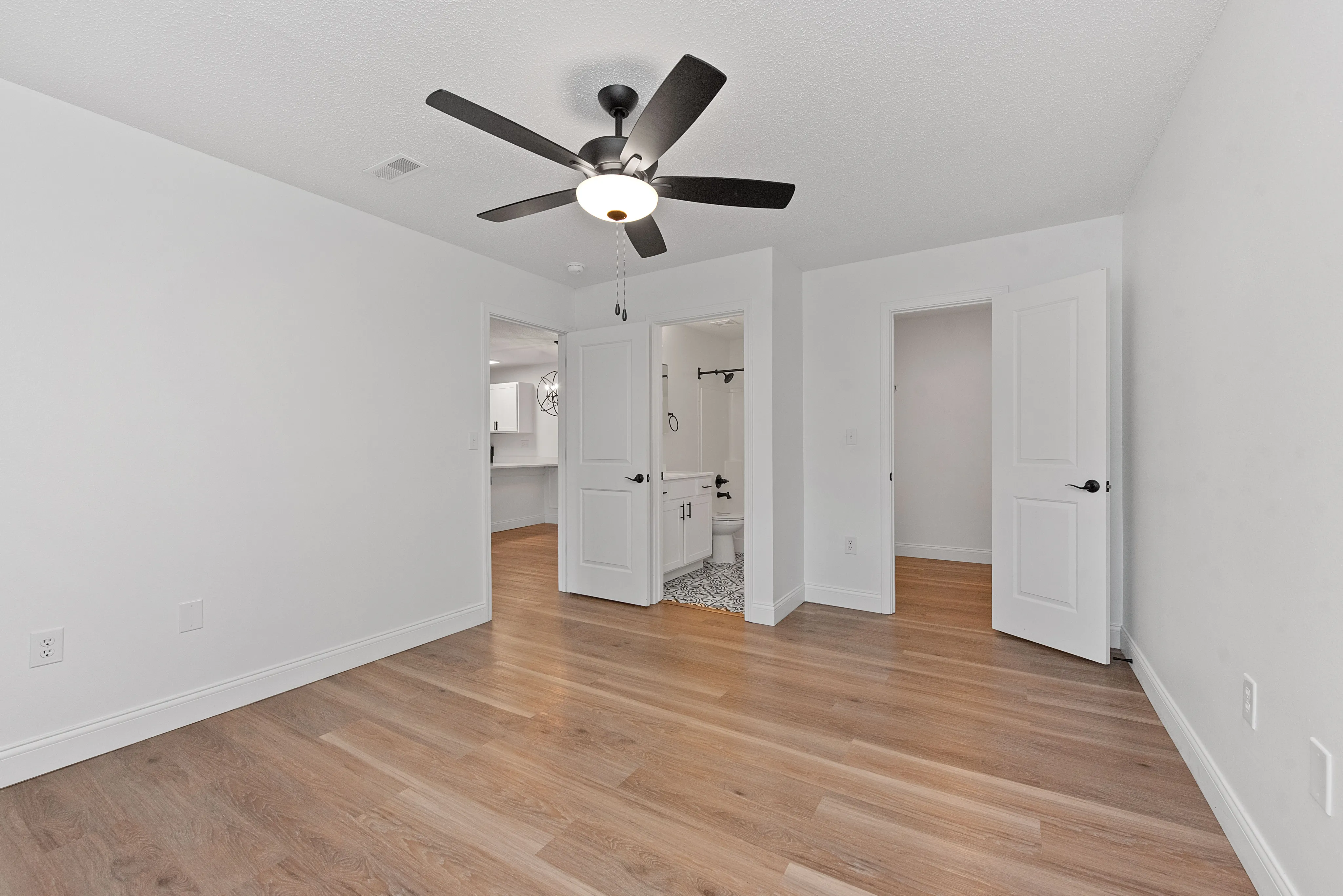 Modern bedroom with elegant wooden flooring, sleek ceiling fan, and bright natural lighting.