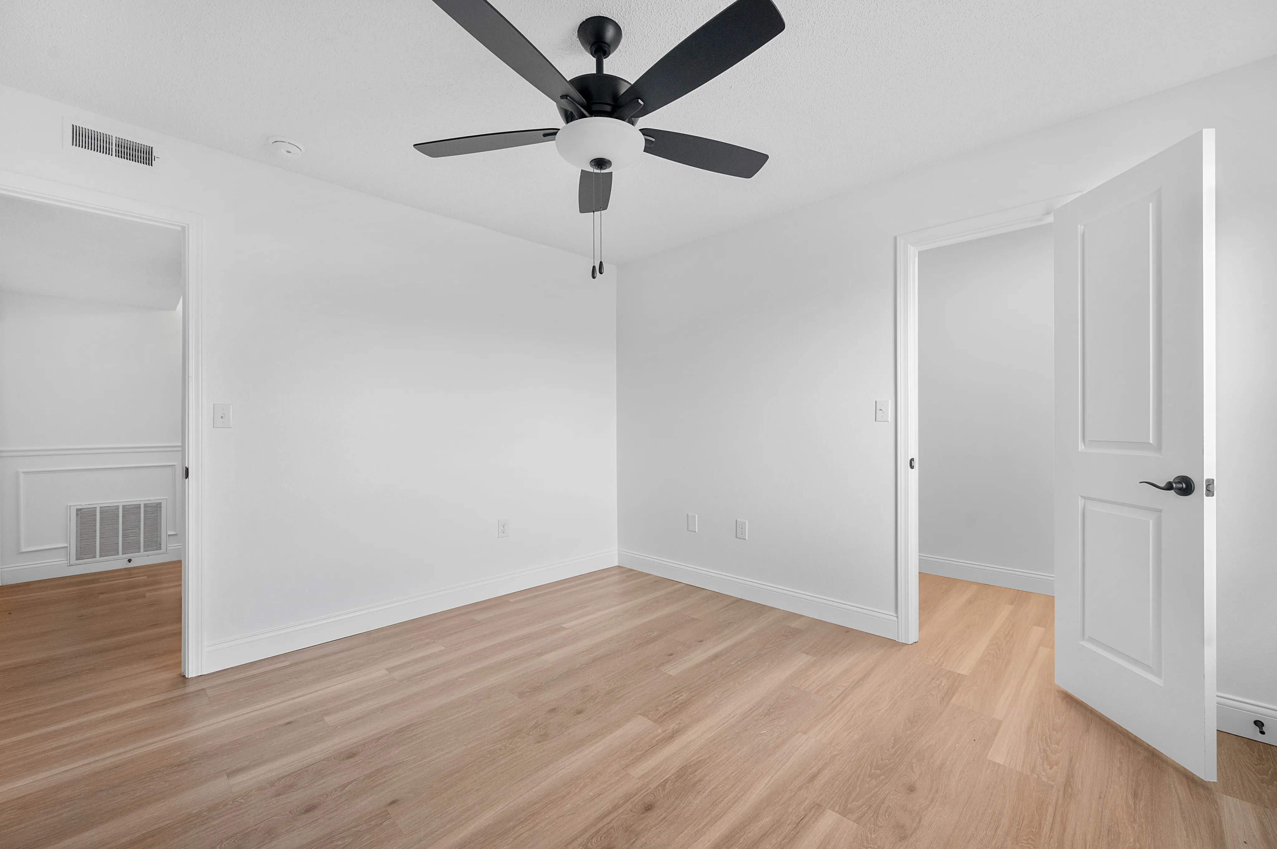 Bright and spacious room with elegant wood flooring and a modern ceiling fan, offering a warm and inviting atmosphere.