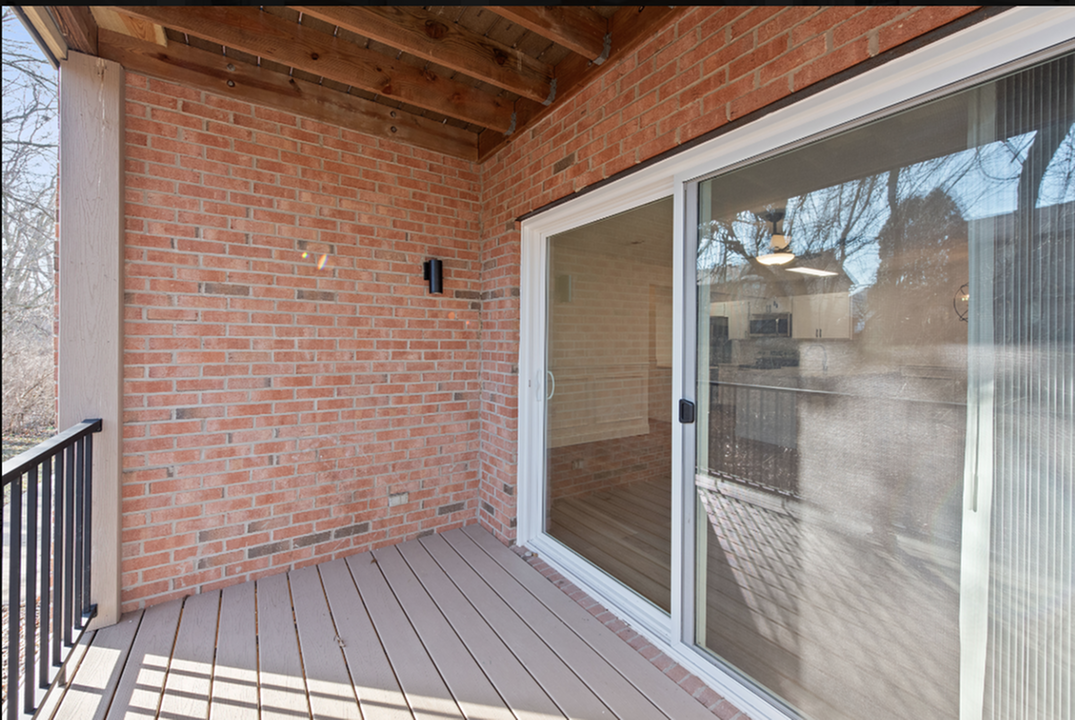 Charming brick-walled balcony with sliding glass door, offering serene views and natural light.