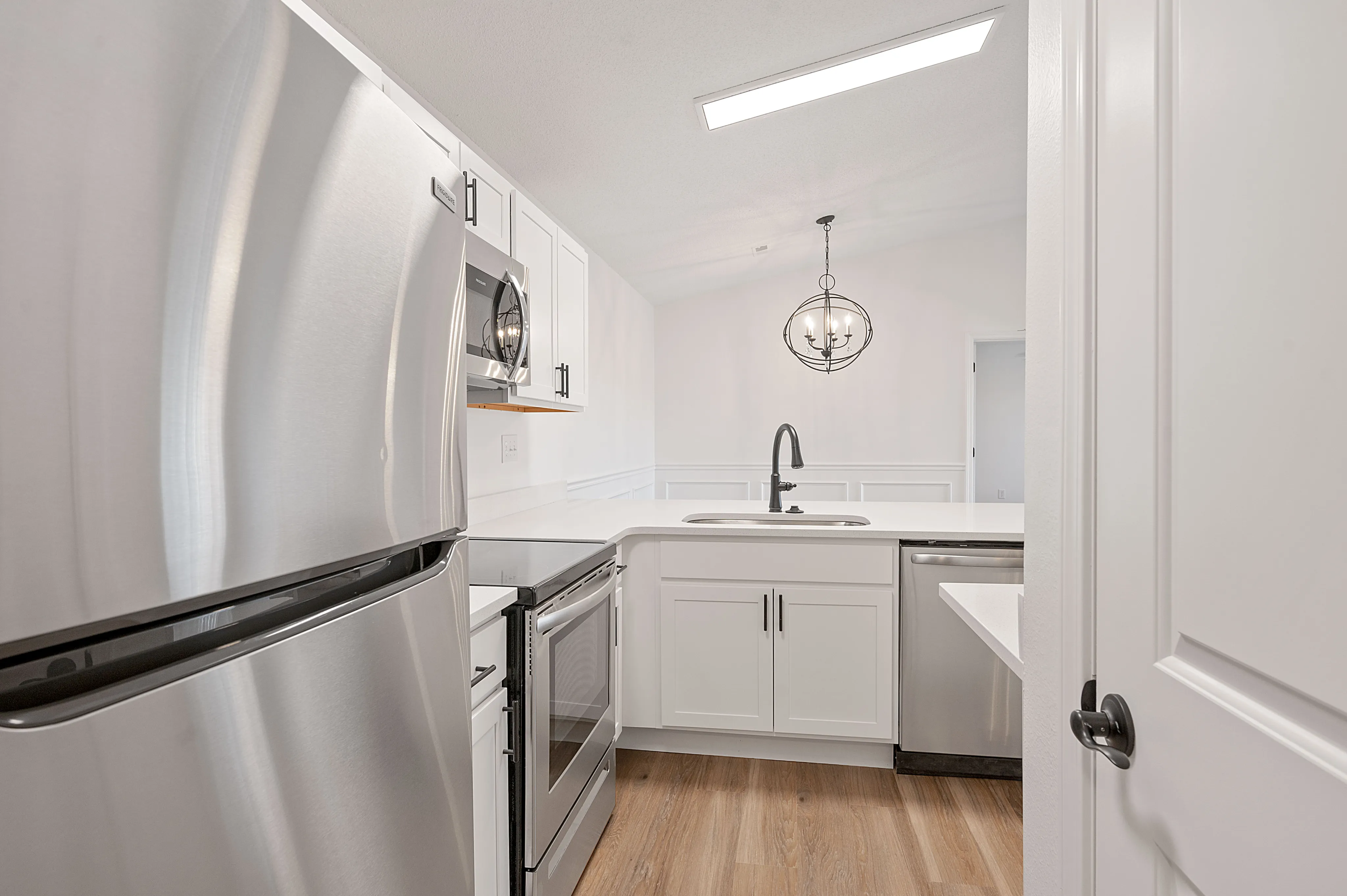 Modern kitchen with sleek stainless steel appliances, elegant lighting, and pristine white cabinetry.