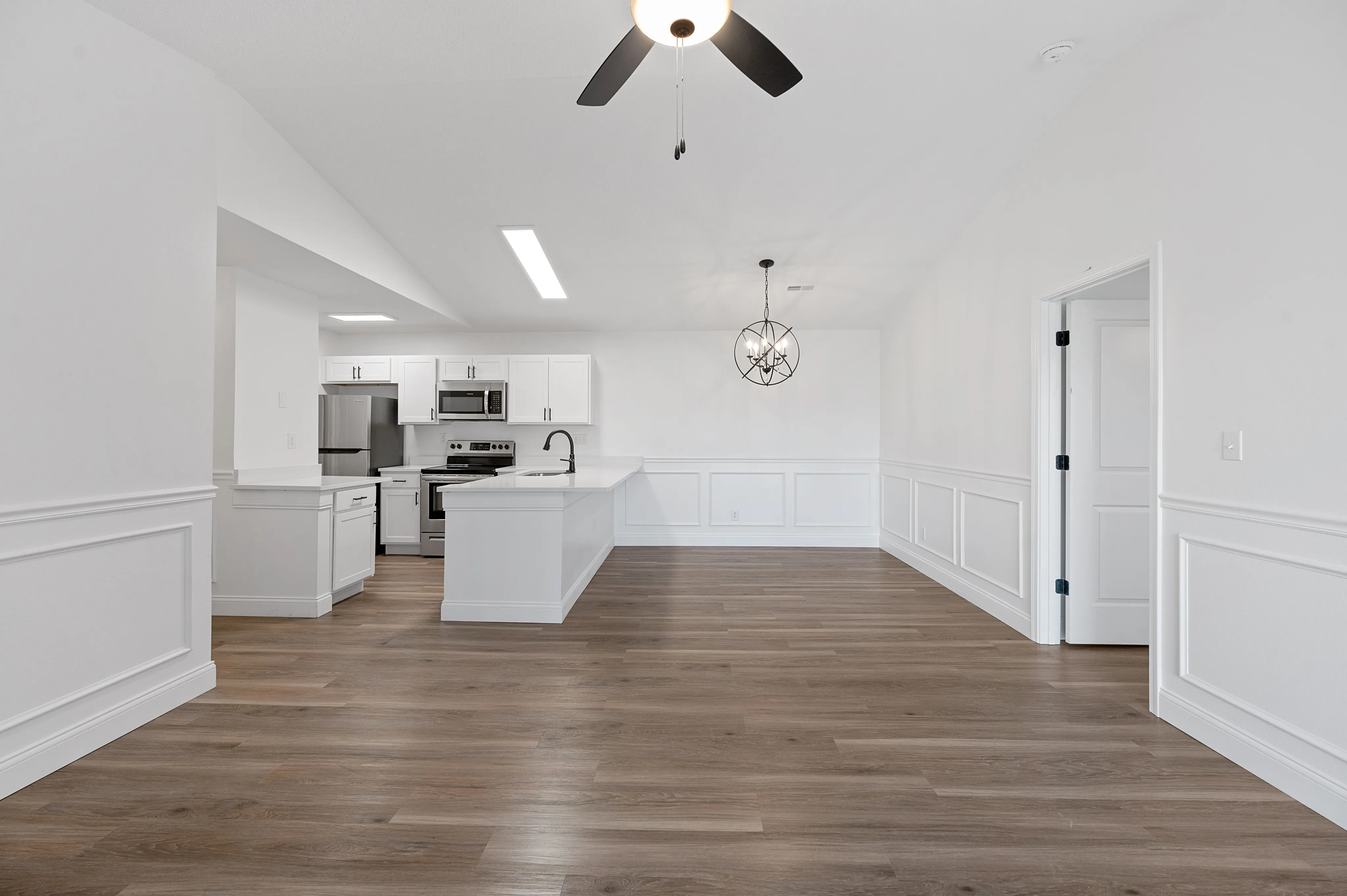 Modern open-concept kitchen and dining area with sleek white cabinets, stainless steel appliances, and elegant wood flooring.