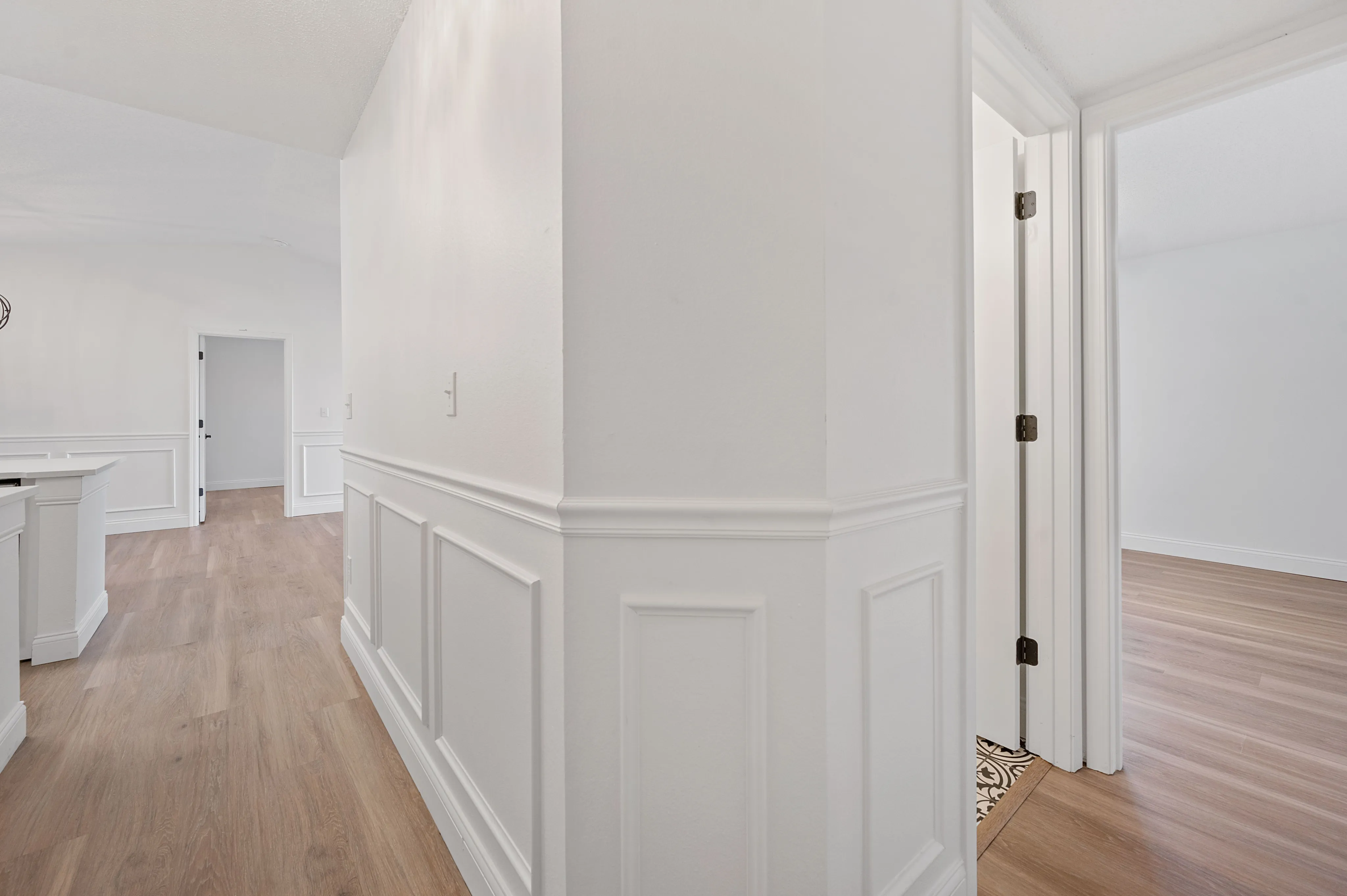 Elegant apartment hallway showcasing pristine white walls, decorative wainscoting, and modern wood flooring leading to spacious rooms.