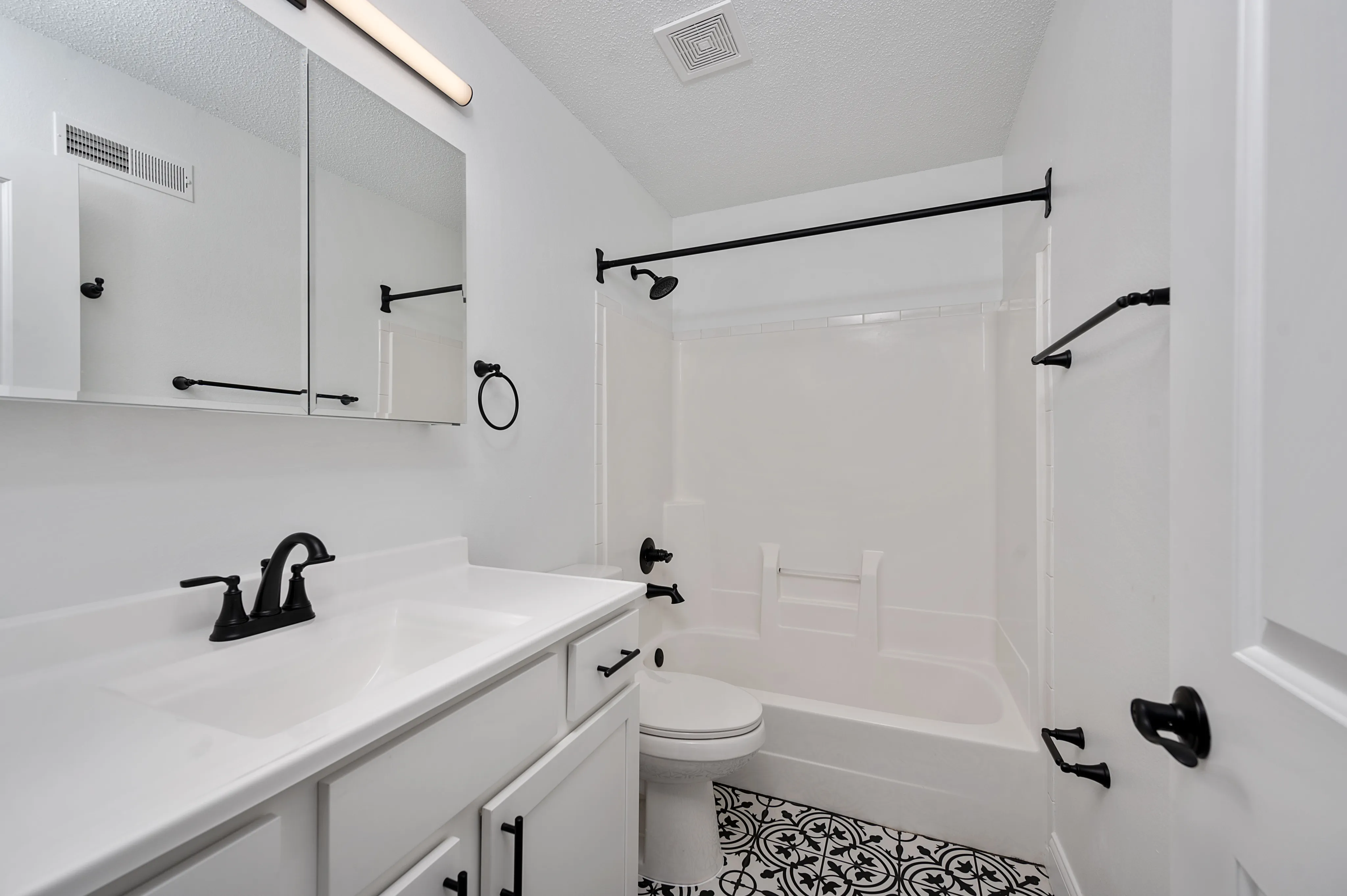 Modern bathroom with white cabinetry, stylish black fixtures, and decorative patterned floor tiles.