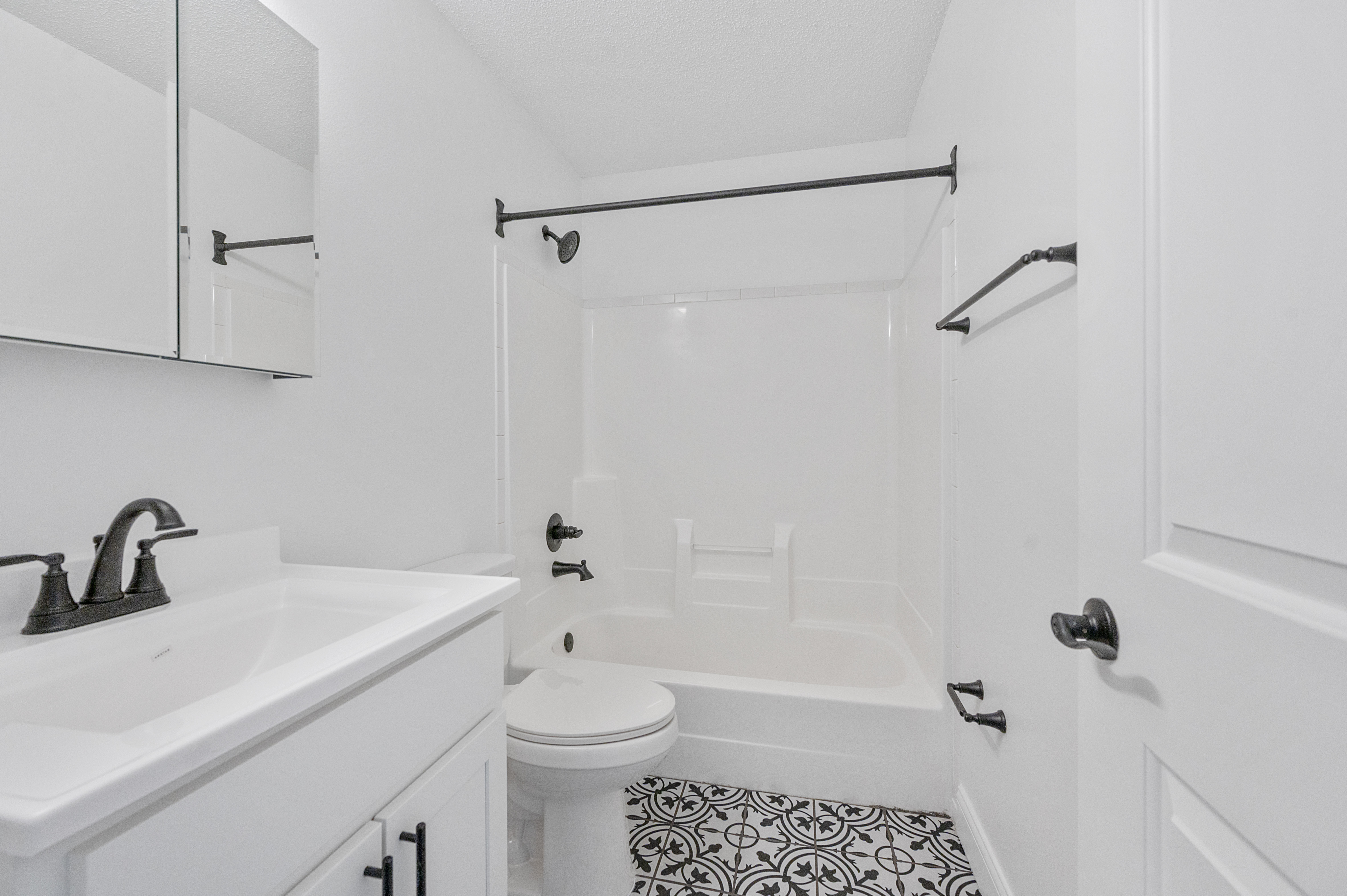 Chic white bathroom featuring modern fixtures, a pristine bathtub, and elegant patterned floor tiles.