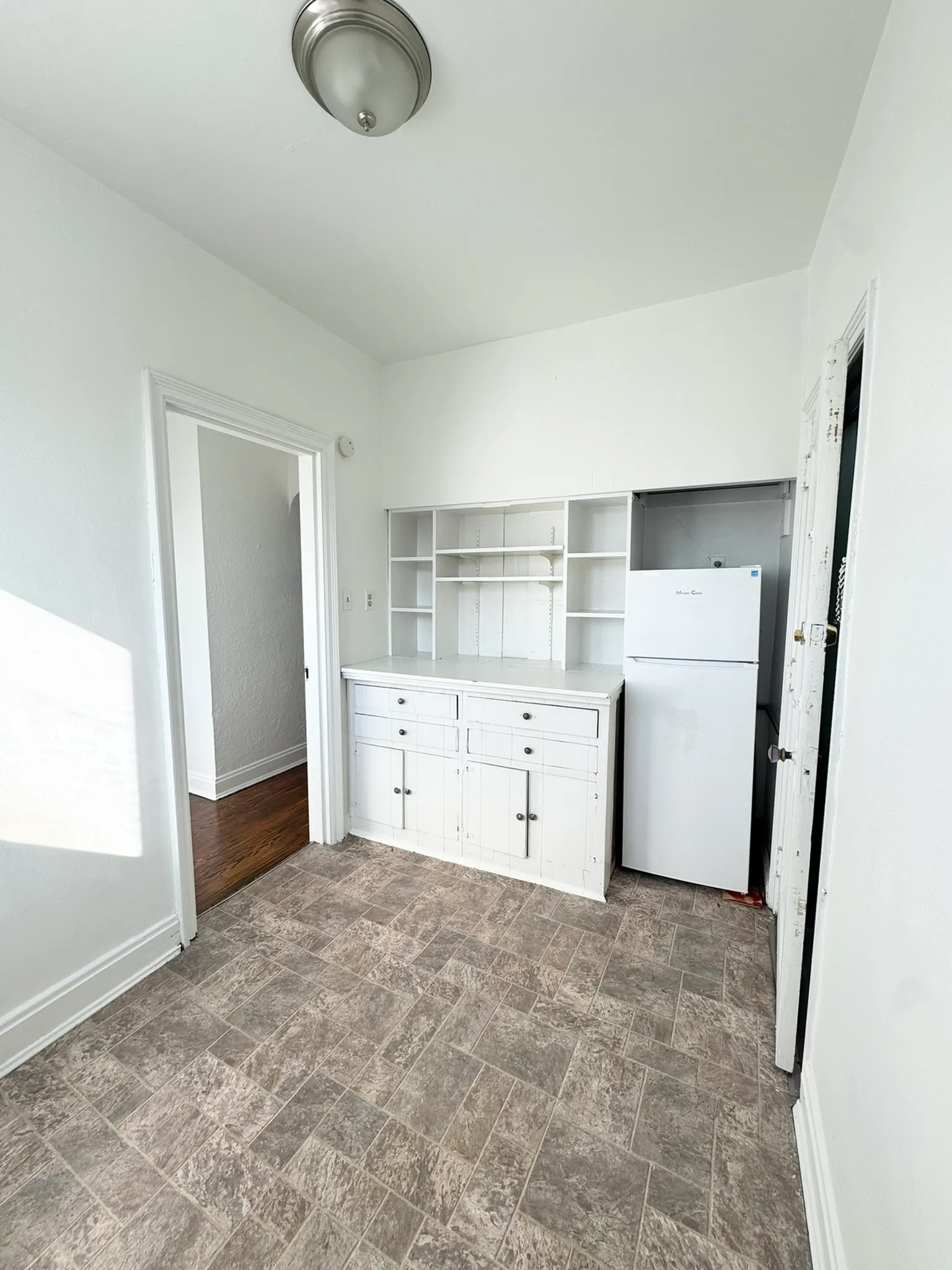 Bright, compact kitchen with white cabinetry and modern flooring, adjacent to a well-lit entryway.