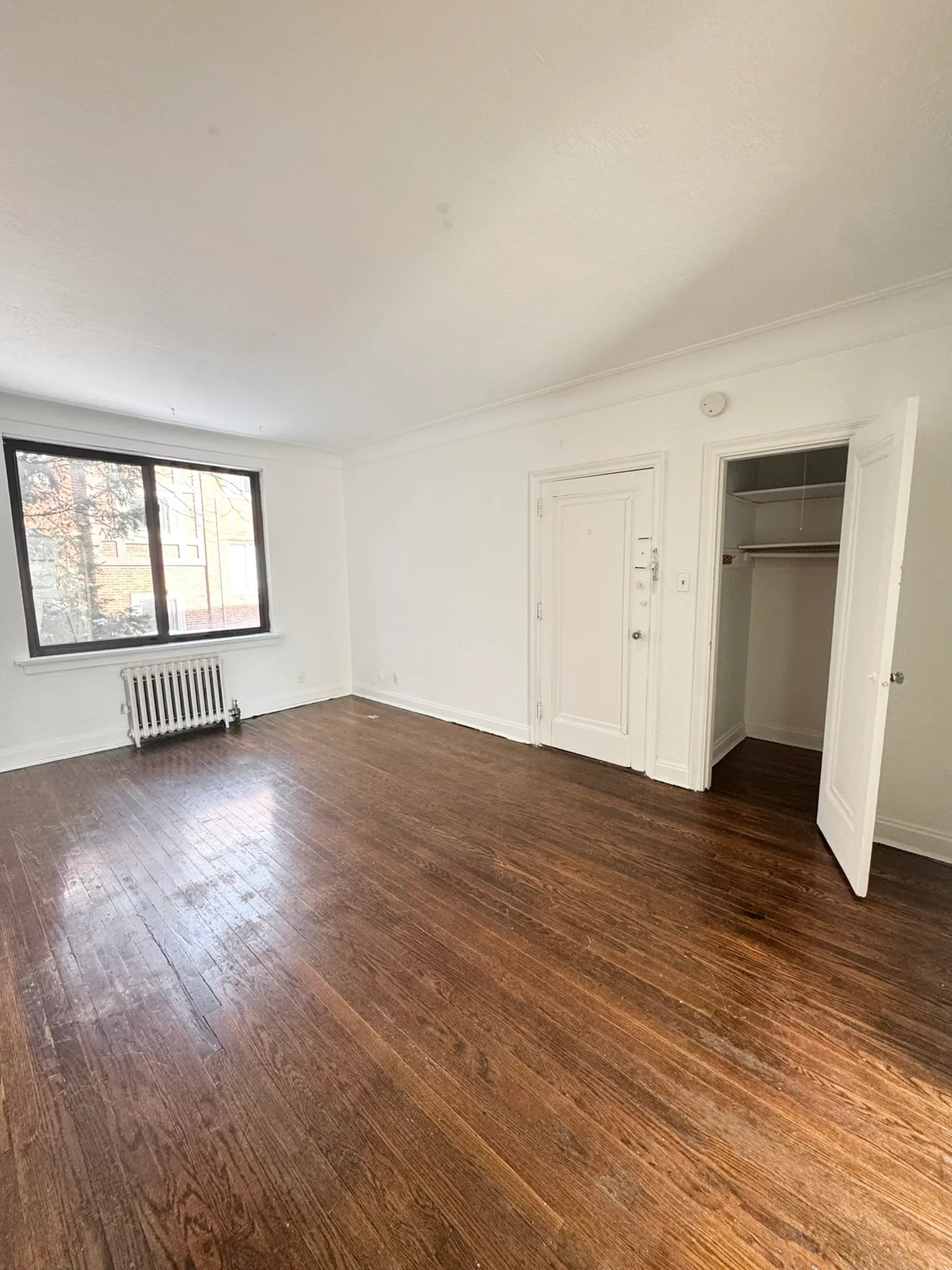 Bright room with elegant wooden floors, large window, and cozy closet space.