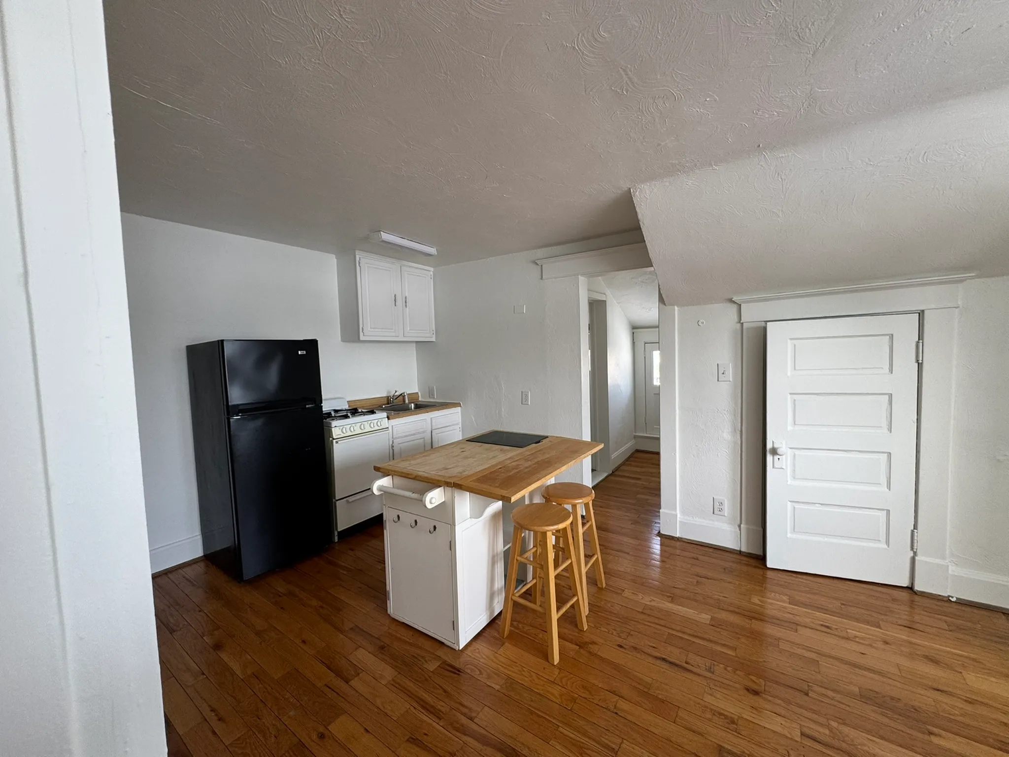 Charming kitchen area with wooden flooring, sleek black fridge, and cozy island with barstools for casual dining.