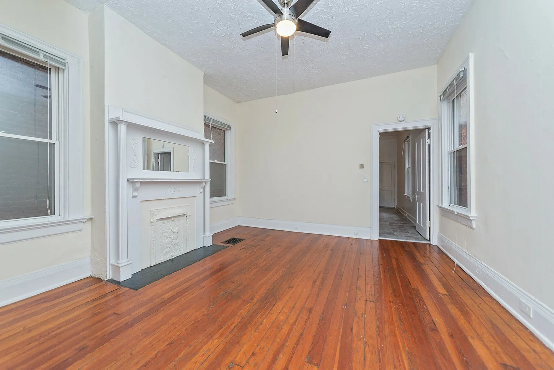 Charming living room with rich hardwood floors, elegant white fireplace, and classic ceiling fan, perfect for cozy gatherings.