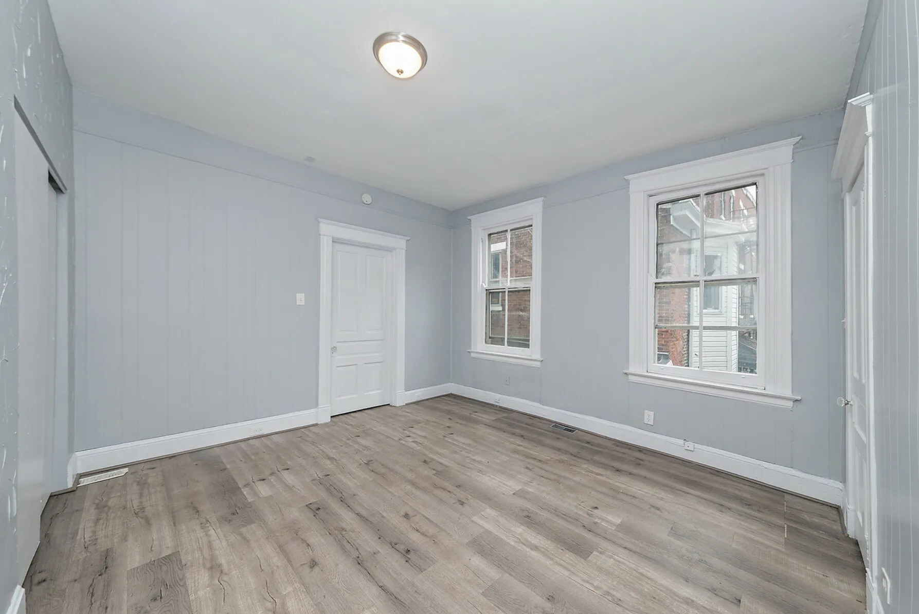 Bright and airy room with elegant laminate flooring, soft gray walls, and abundant natural light from double windows.