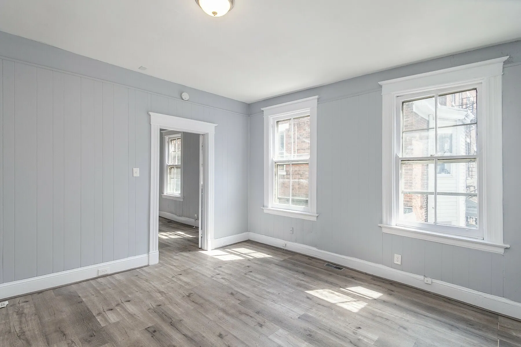 Bright and airy room with large windows, elegant wood flooring, and modern gray panel walls.
