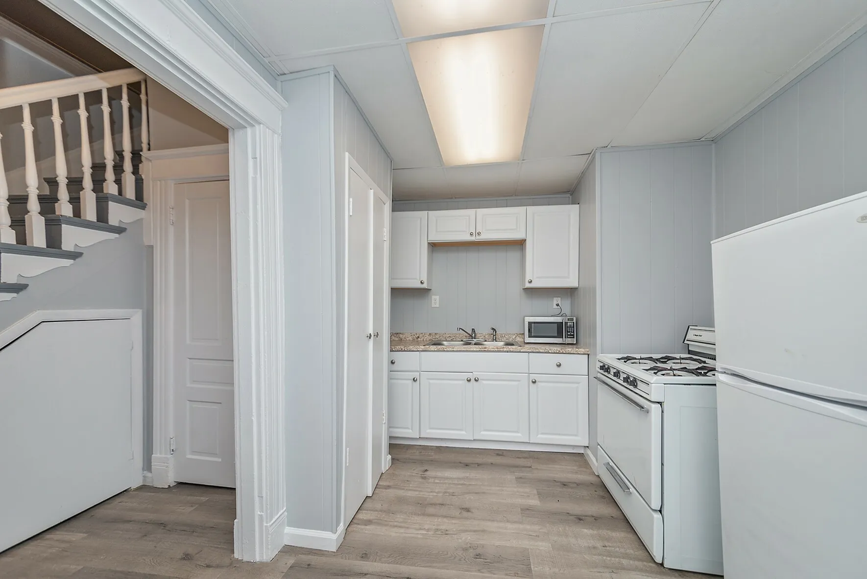 Charming kitchen with modern appliances, sleek white cabinets, and elegant wood flooring adjacent to a stylish staircase.