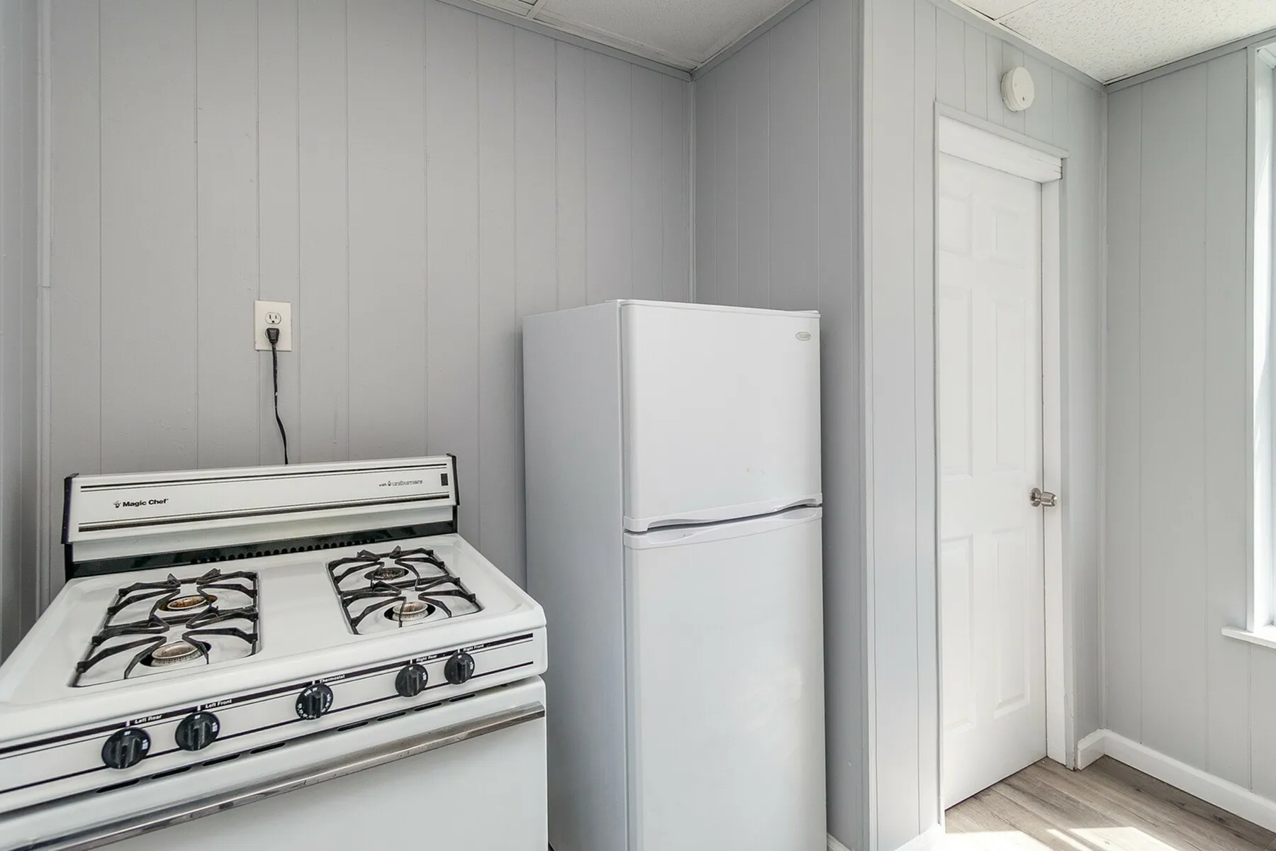 Charming kitchen corner featuring a classic white gas stove and an elegant refrigerator, set against soft gray paneling for a cozy feel.