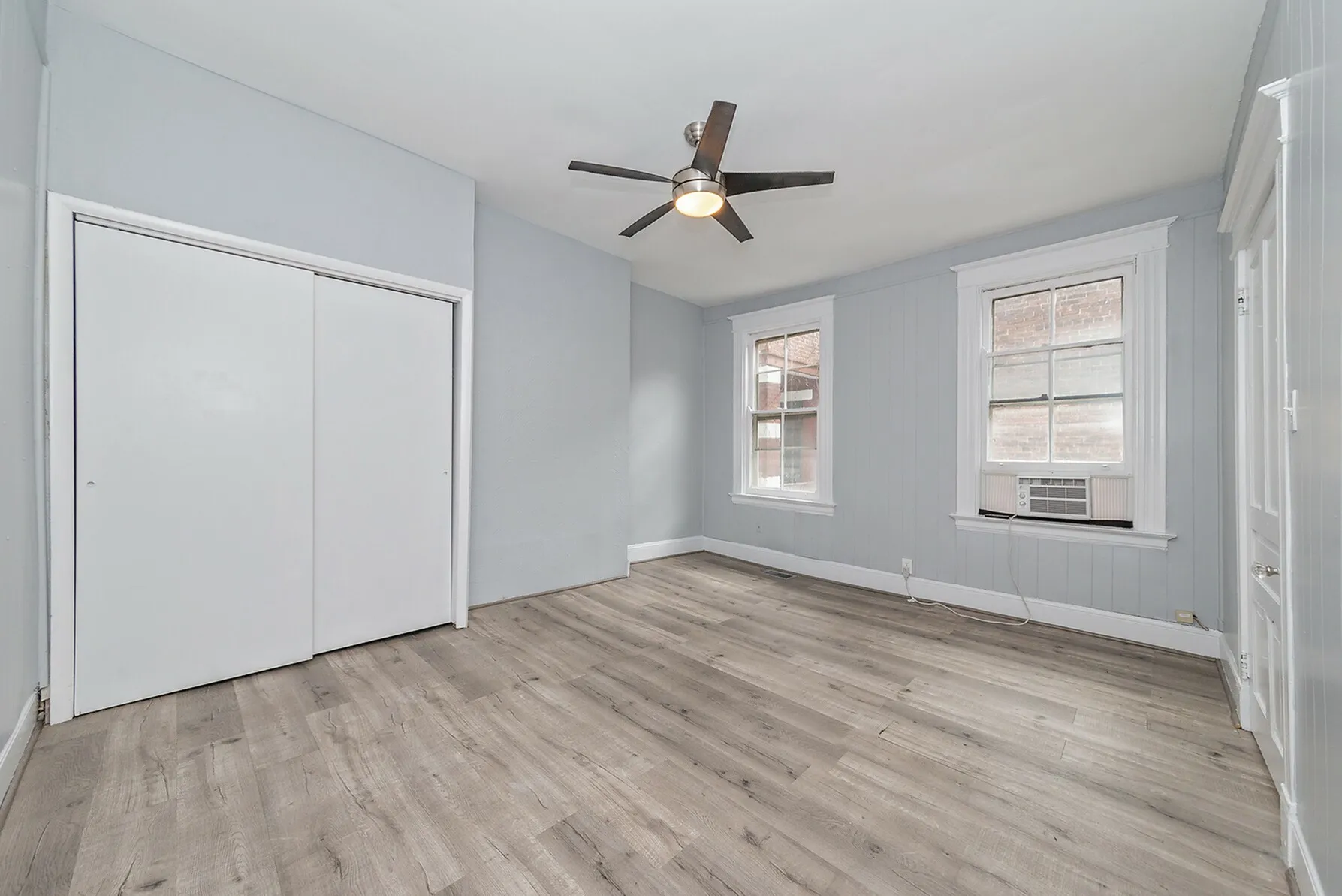 Bright and airy room with modern laminate flooring, featuring a sleek ceiling fan and large windows.