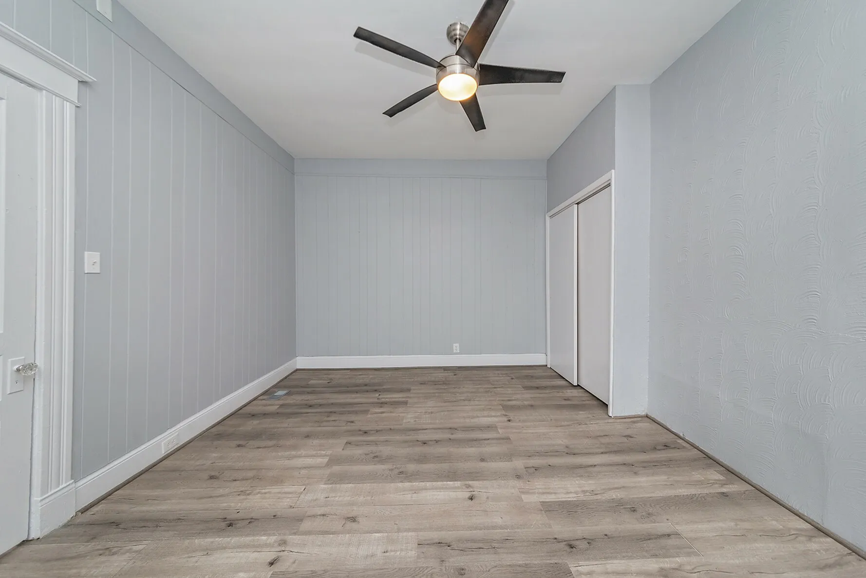 Sleek modern room with elegant wooden flooring, stylish ceiling fan, and soothing grey walls offering a spacious and versatile living area.