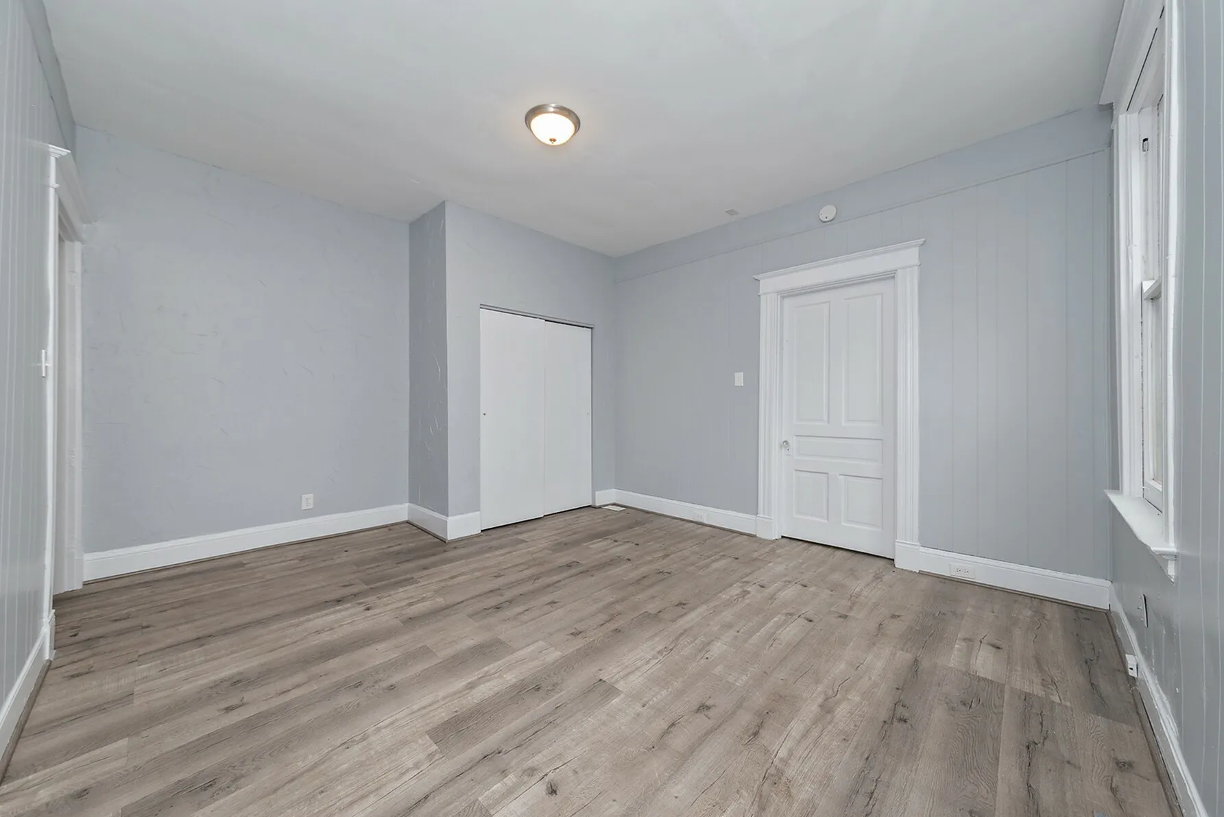 Bright and spacious room with modern wood flooring and light gray walls, featuring elegant white trim and a cozy ambiance.