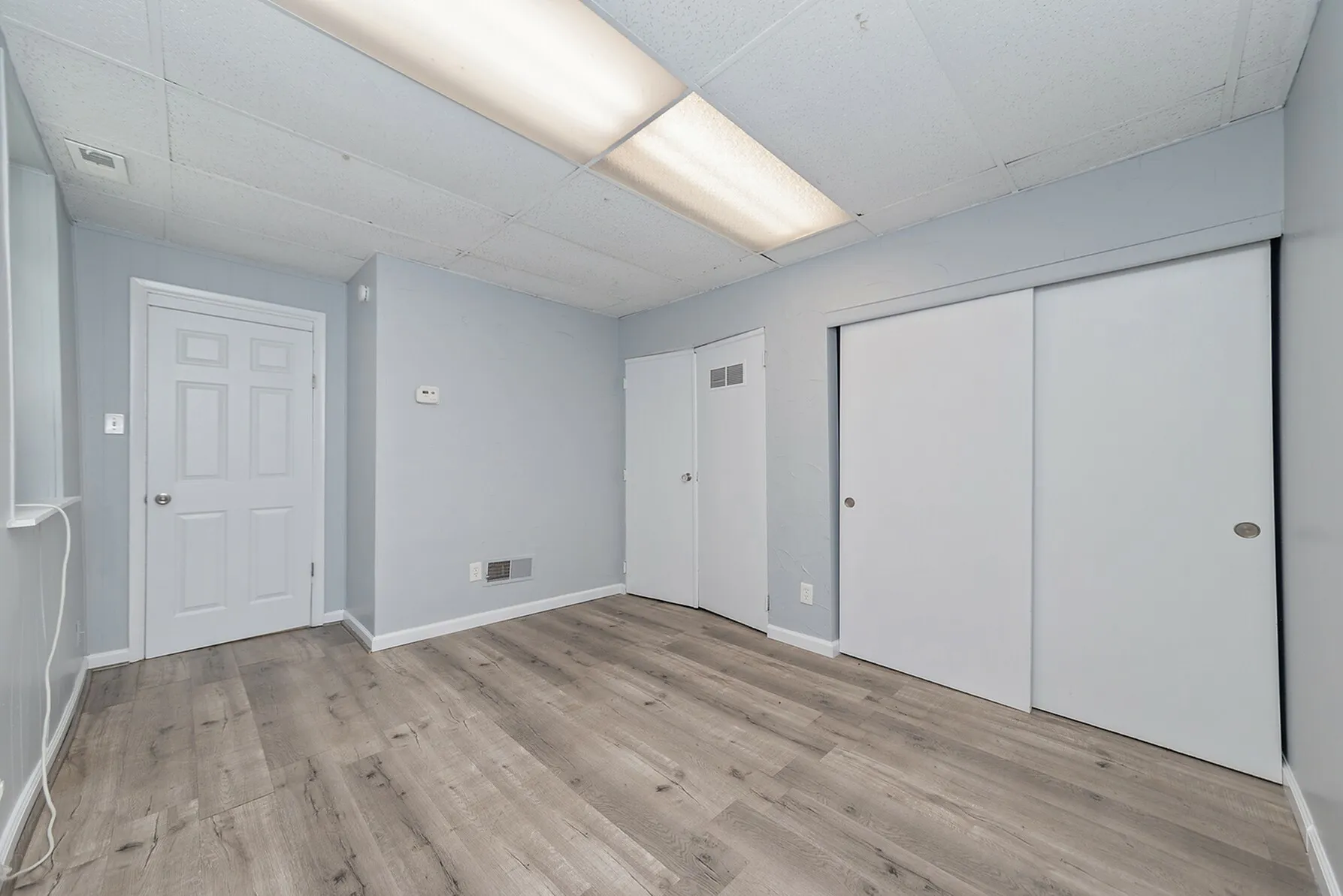 Bright and modern room with sleek wood flooring, fresh grey walls, and ample closet space.
