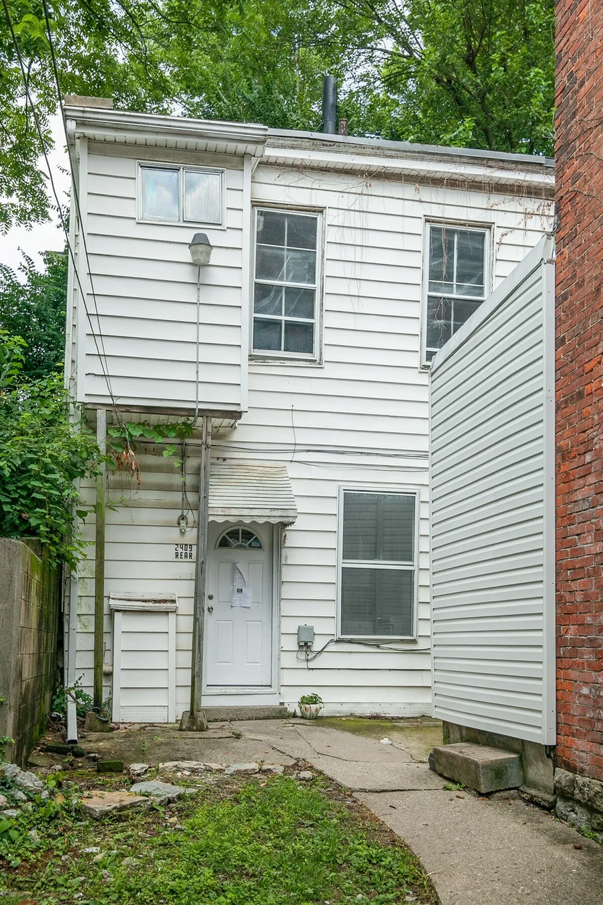 Charming two-story white house with a quaint entrance, nestled between greenery and brickwork, offering a cozy and private living space.