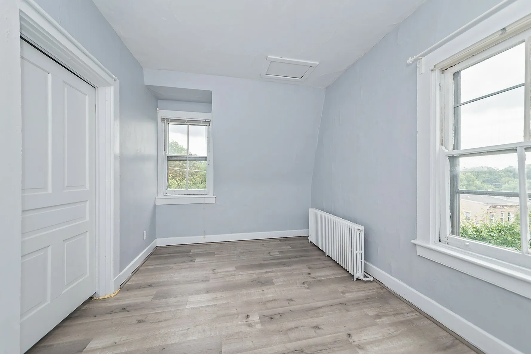 Bright, cozy room with large windows, freshly painted walls, and stylish wood flooring, highlighting serene natural views.