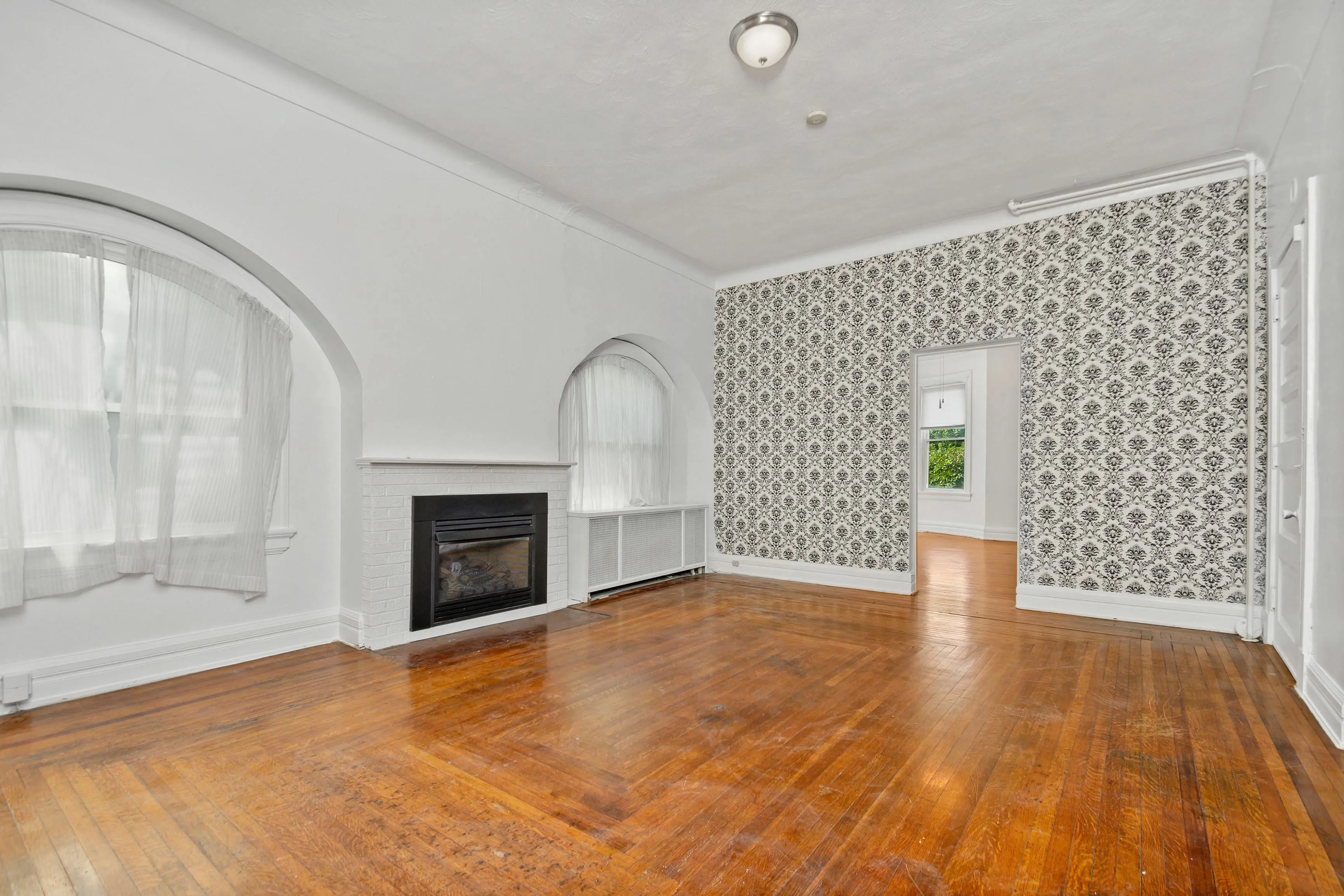 Charming living room with elegant arched windows, classic fireplace, and beautifully patterned accent wall.